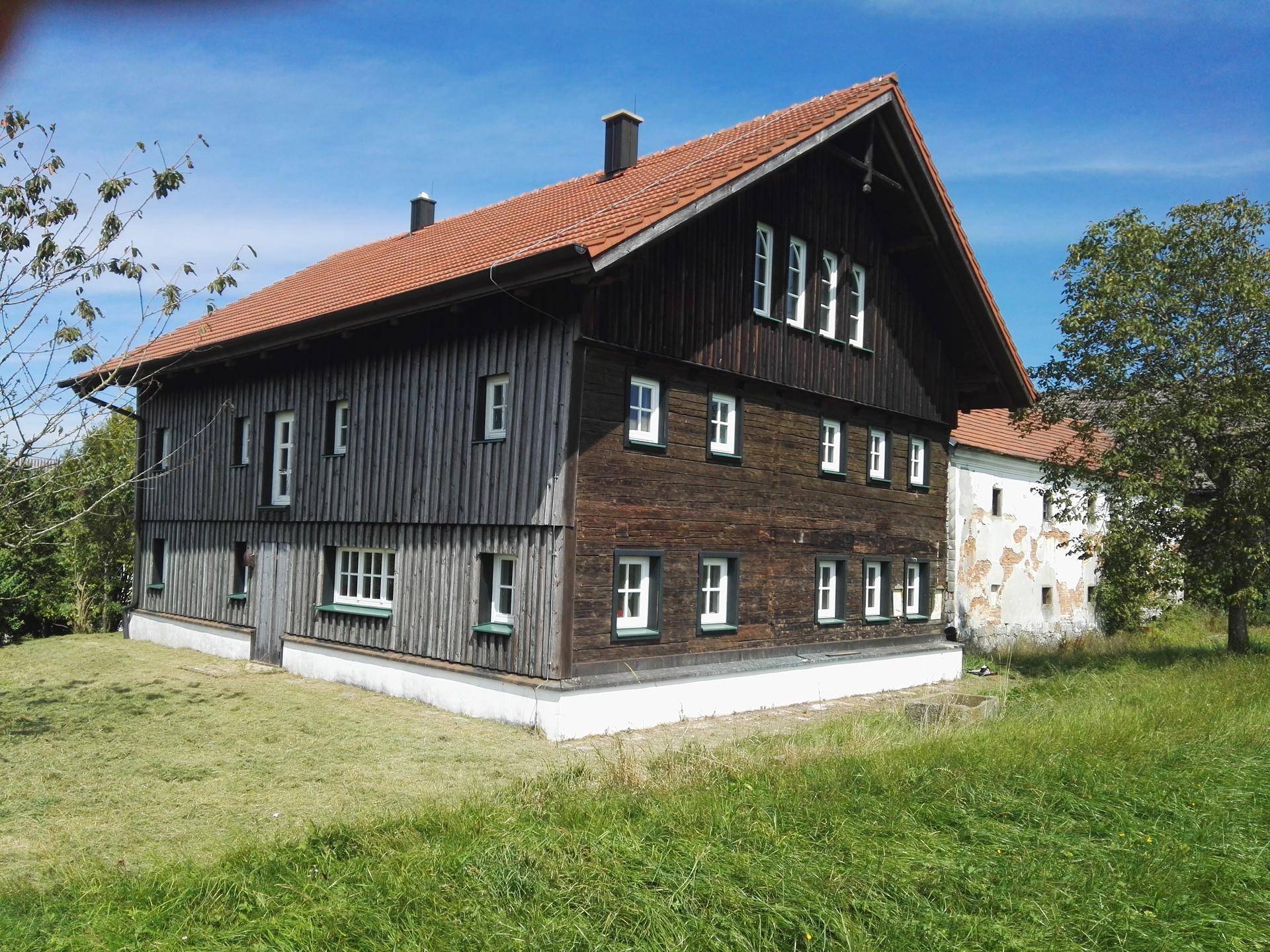 Charmantes Holzhaus mit rotem Ziegeldach und grüner Wiese unter blauem Himmel.