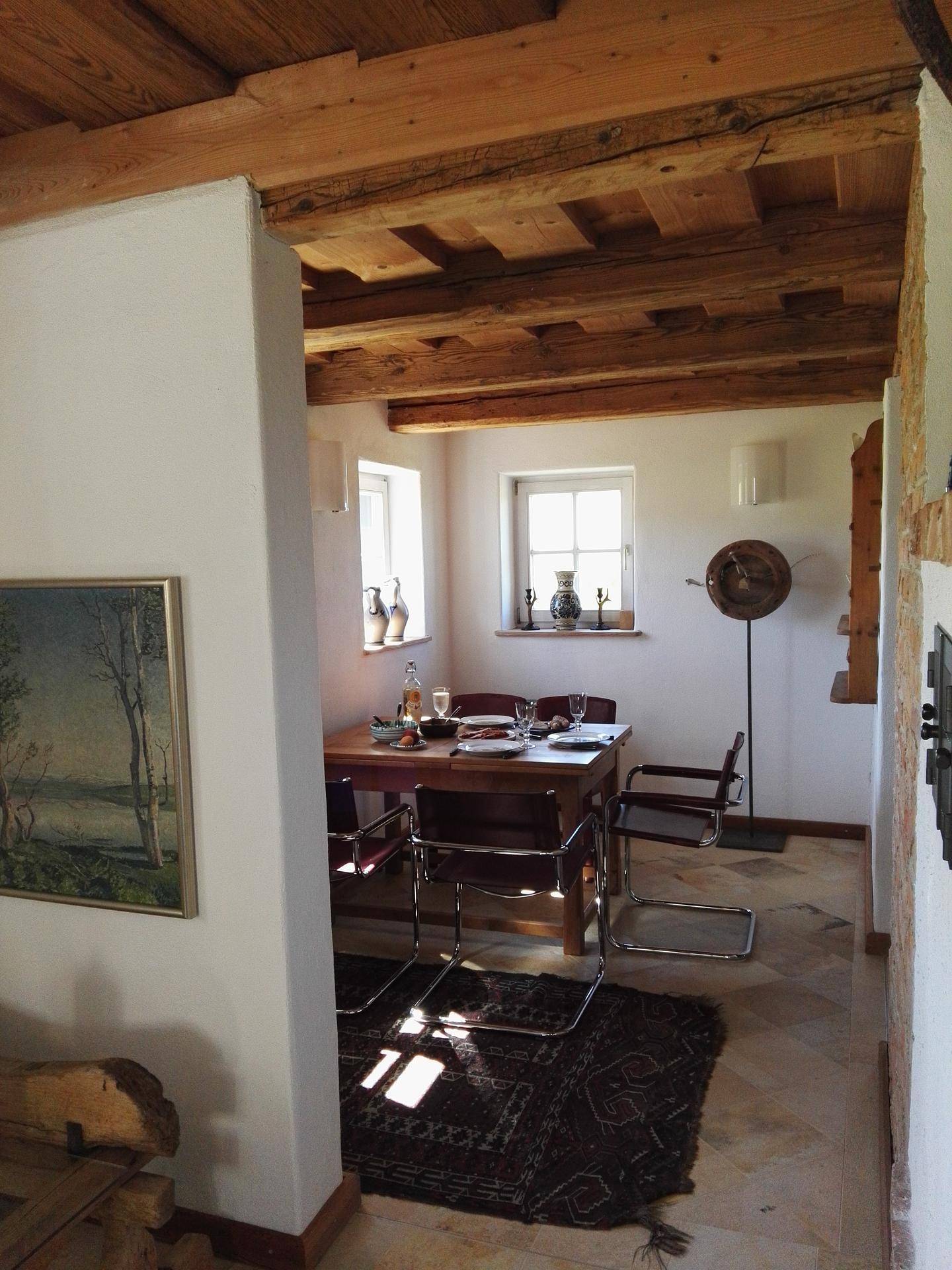 Heller Essbereich mit Holztisch, Fliesenboden und sichtbaren Deckenbalken.