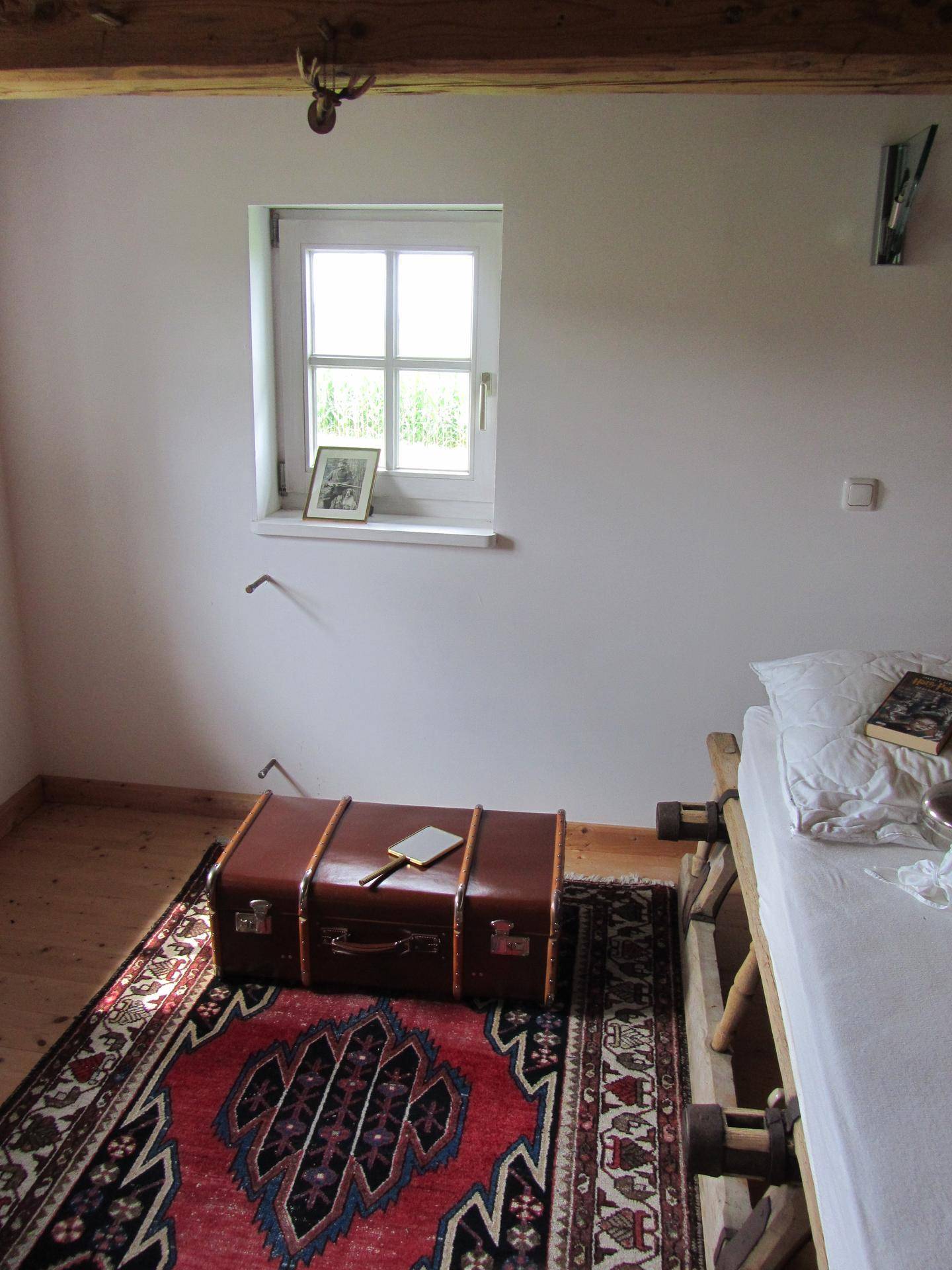 Gemütliches Schlafzimmer mit Einzelbett, Holzboden und einem Fenster mit Tageslicht.