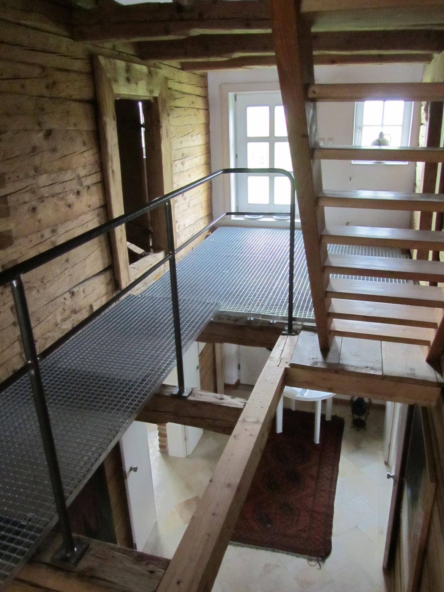 Offener Flurbereich mit Holztreppe, Metallgitterboden und rustikalen Holzwänden.