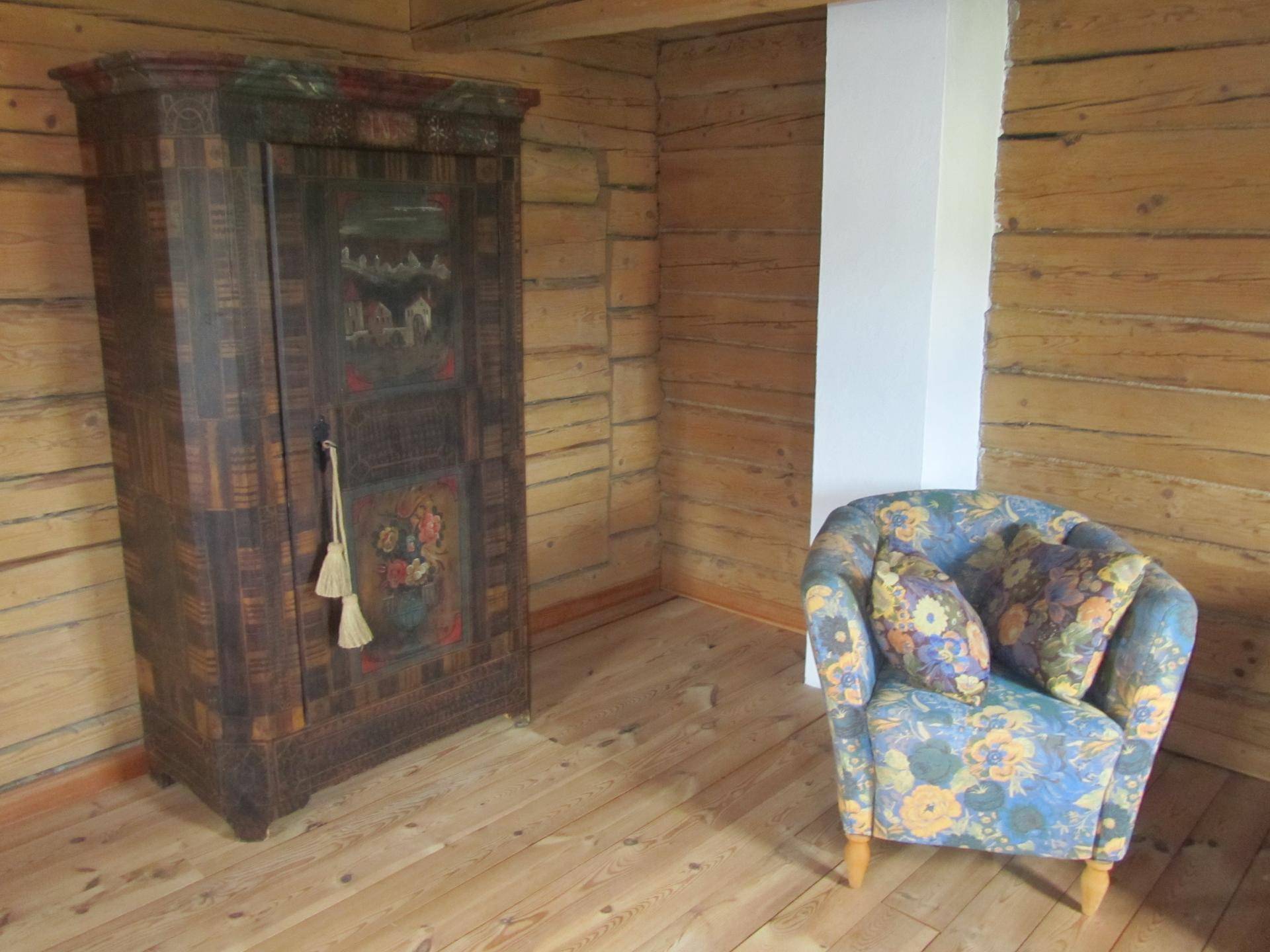 Rustikaler Wohnraum mit Holzwänden, bemaltem Schrank und floralem Sessel.