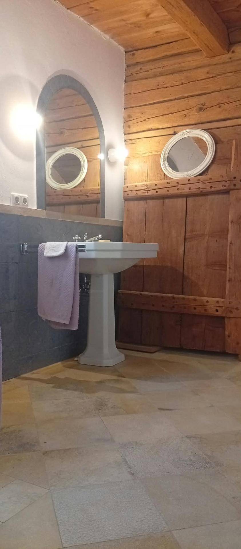 Badezimmer mit Standwaschbecken, großem Bogenspiegel und rustikalen Holzvertäfelungen an den Wänden.