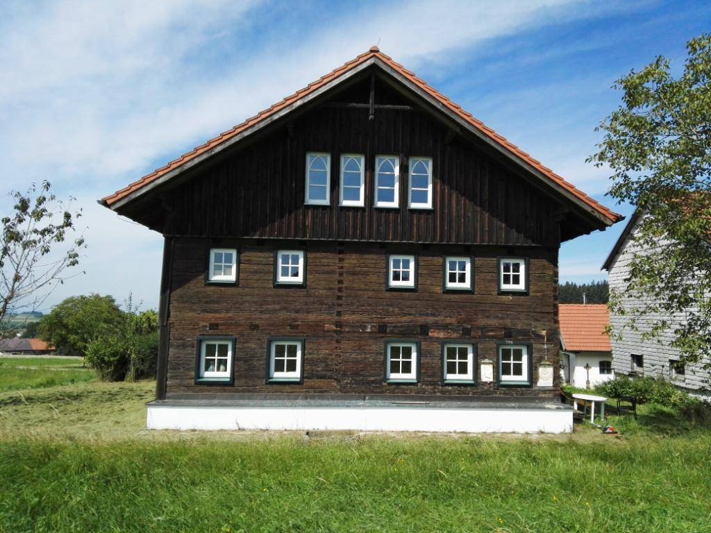Traditionelles Holzhaus mit Satteldach und vielen Fenstern in ländlicher Umgebung.