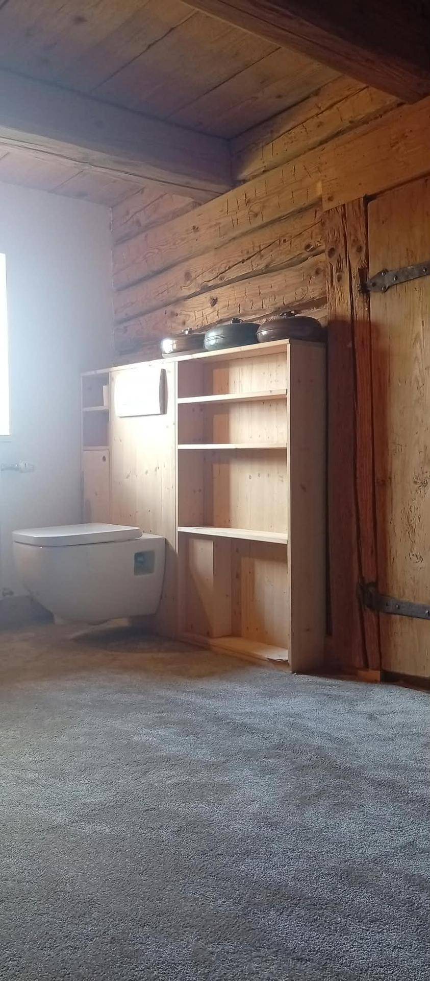 WC-Bereich mit Holzwänden, Teppichboden und einem praktischen Holzregal.