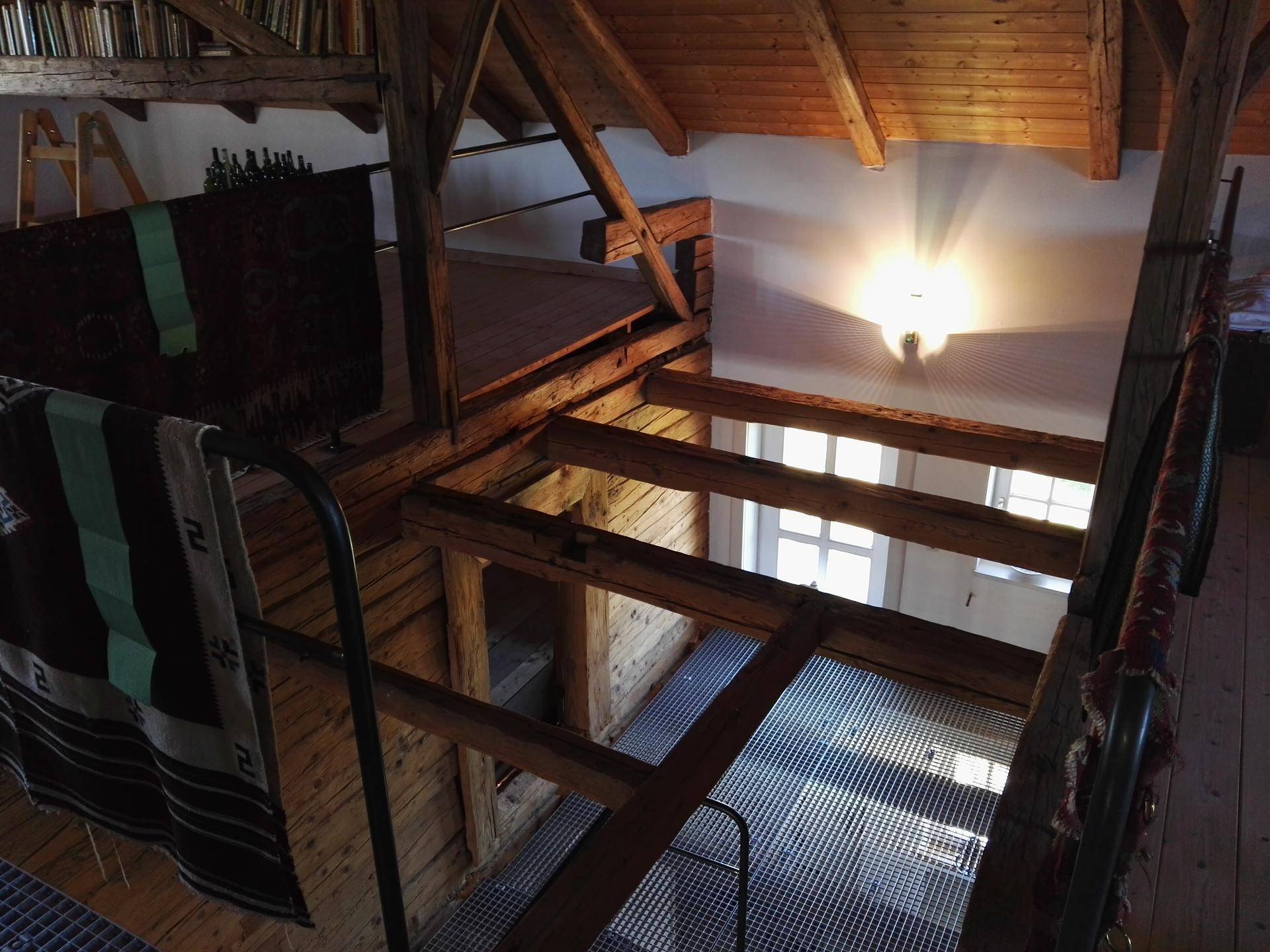 Blick von oben auf eine offene Galerie mit Metallgitterboden und Holzbalkenkonstruktion.