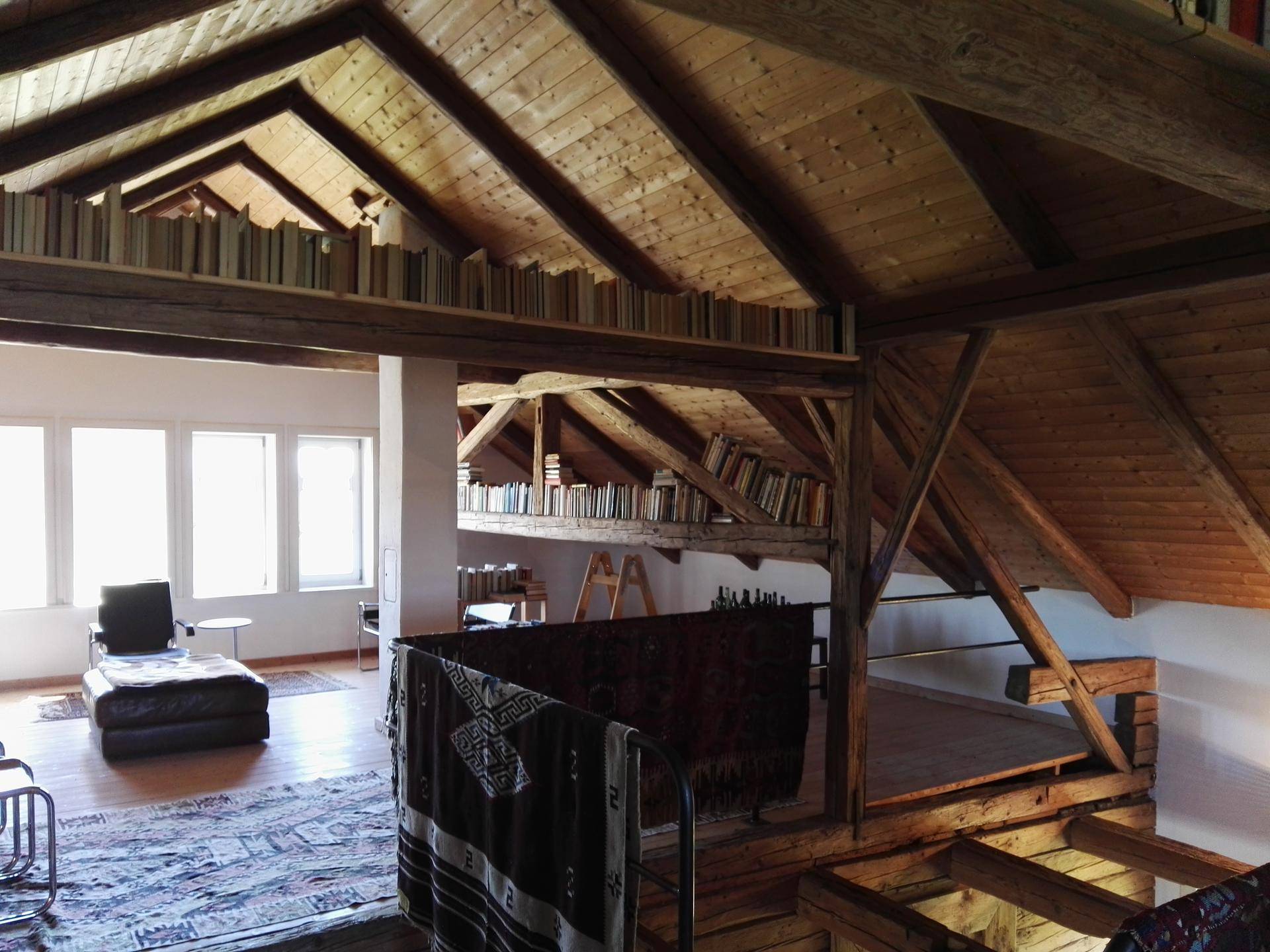 Weitläufige Galerie im Dachgeschoss mit Holzbalken, Bücherregalen und Blick in den unteren Bereich.