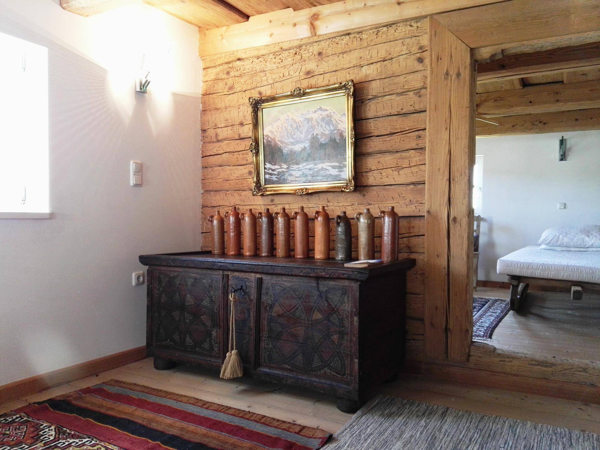 Rustikaler Flur mit Holzwänden, alter Truhe und Blick in ein angrenzendes Schlafzimmer.