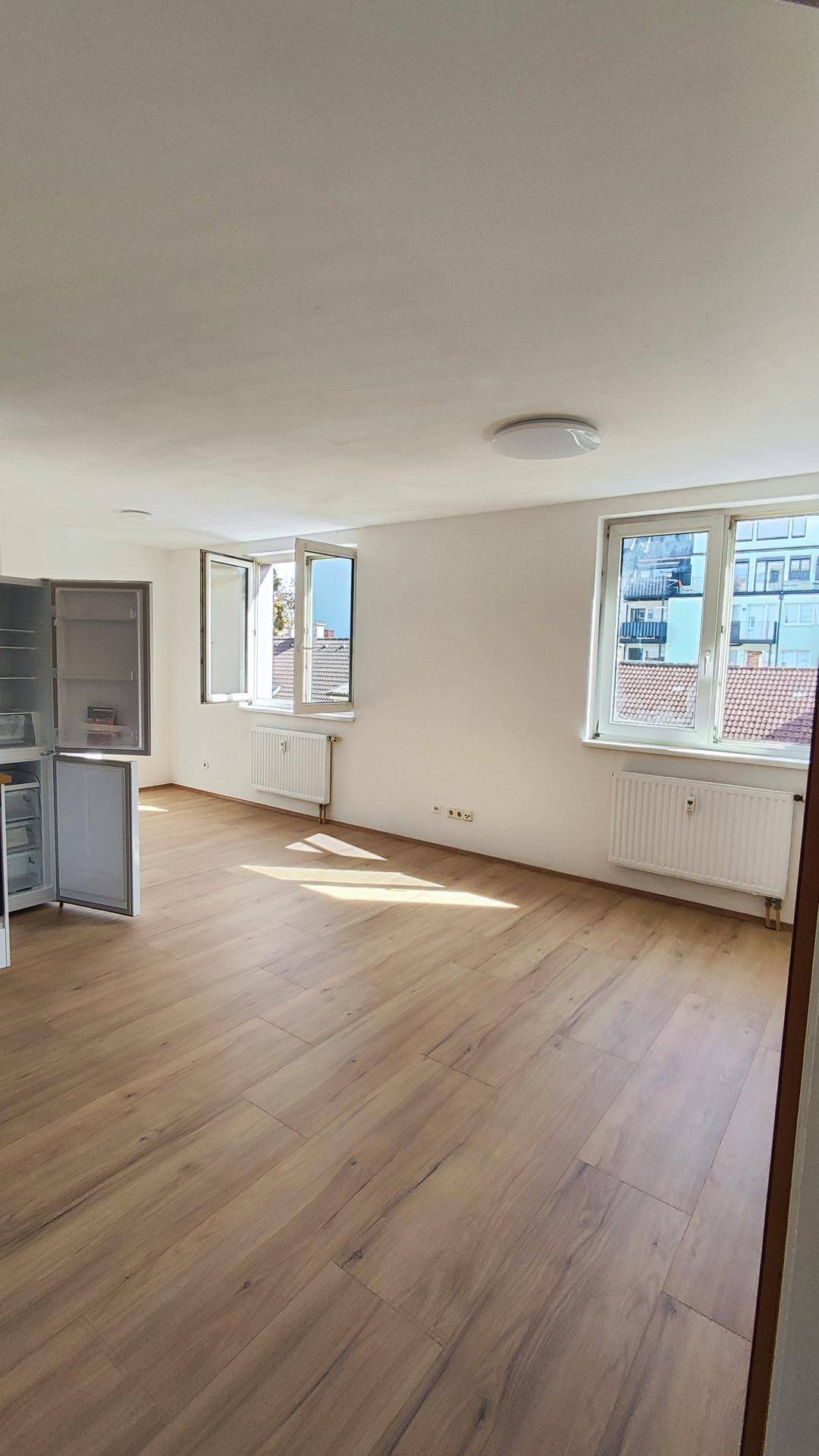 Geräumiger Wohnbereich mit Laminatboden, großen Fenstern und viel natürlichem Lichteinfall.
