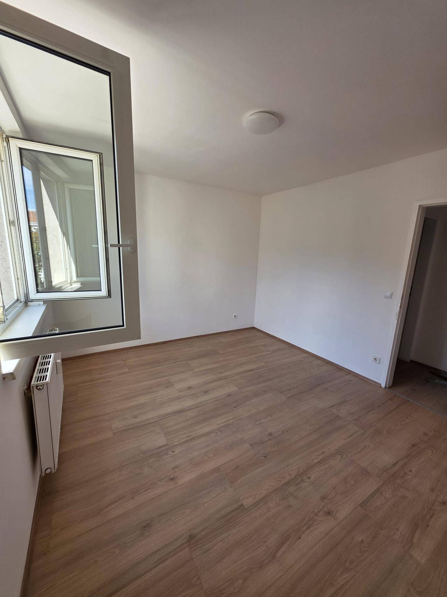 Helles Schlafzimmer mit Laminatboden und einem großen Fenster, das viel Tageslicht spendet.