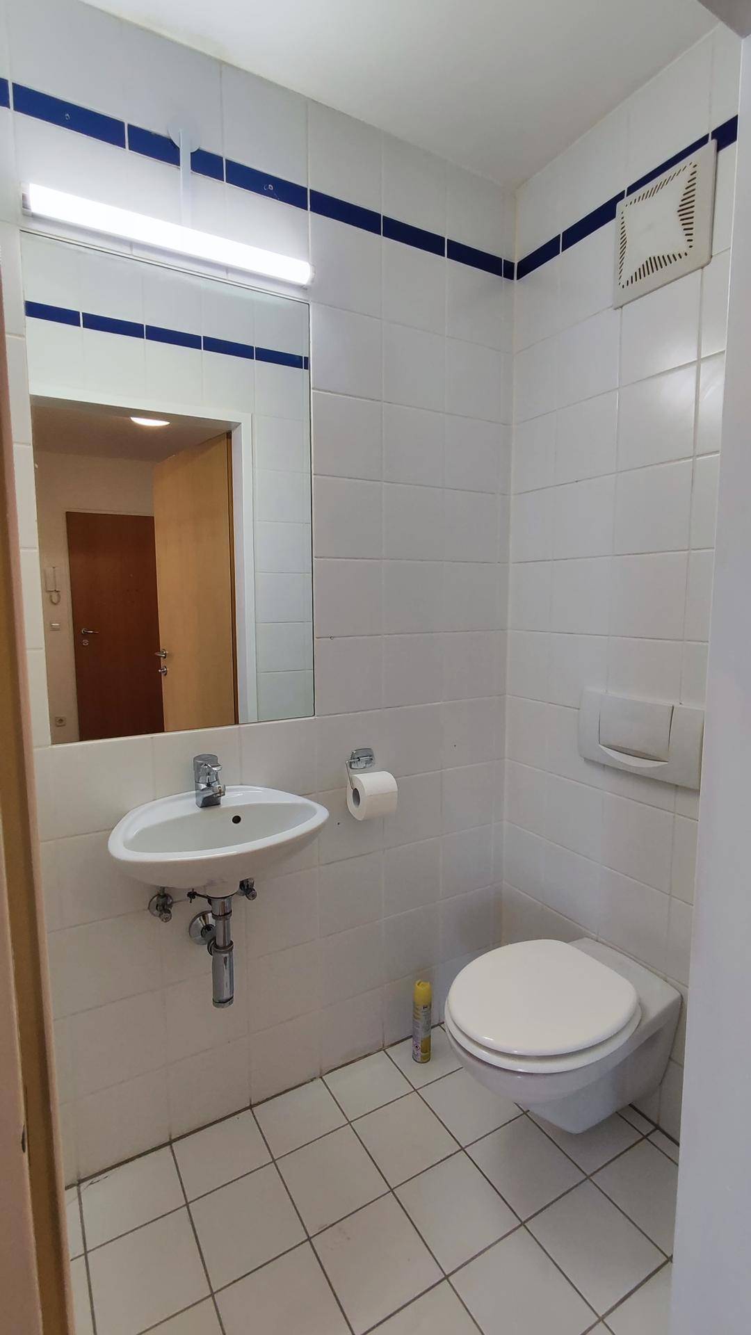 Kleines Gäste-WC mit weißen Fliesen, Waschbecken und Wand-WC, akzentuiert durch blaue Bordüre.