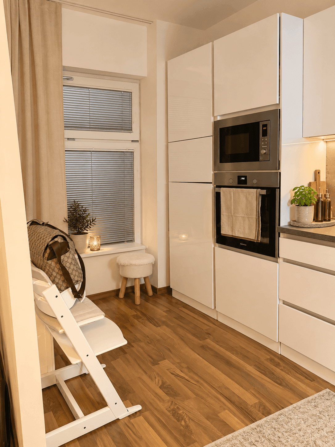 Moderne Küche mit weißen Hochglanzschränken, integriertem Backofen und Mikrowelle sowie einem Fenster.