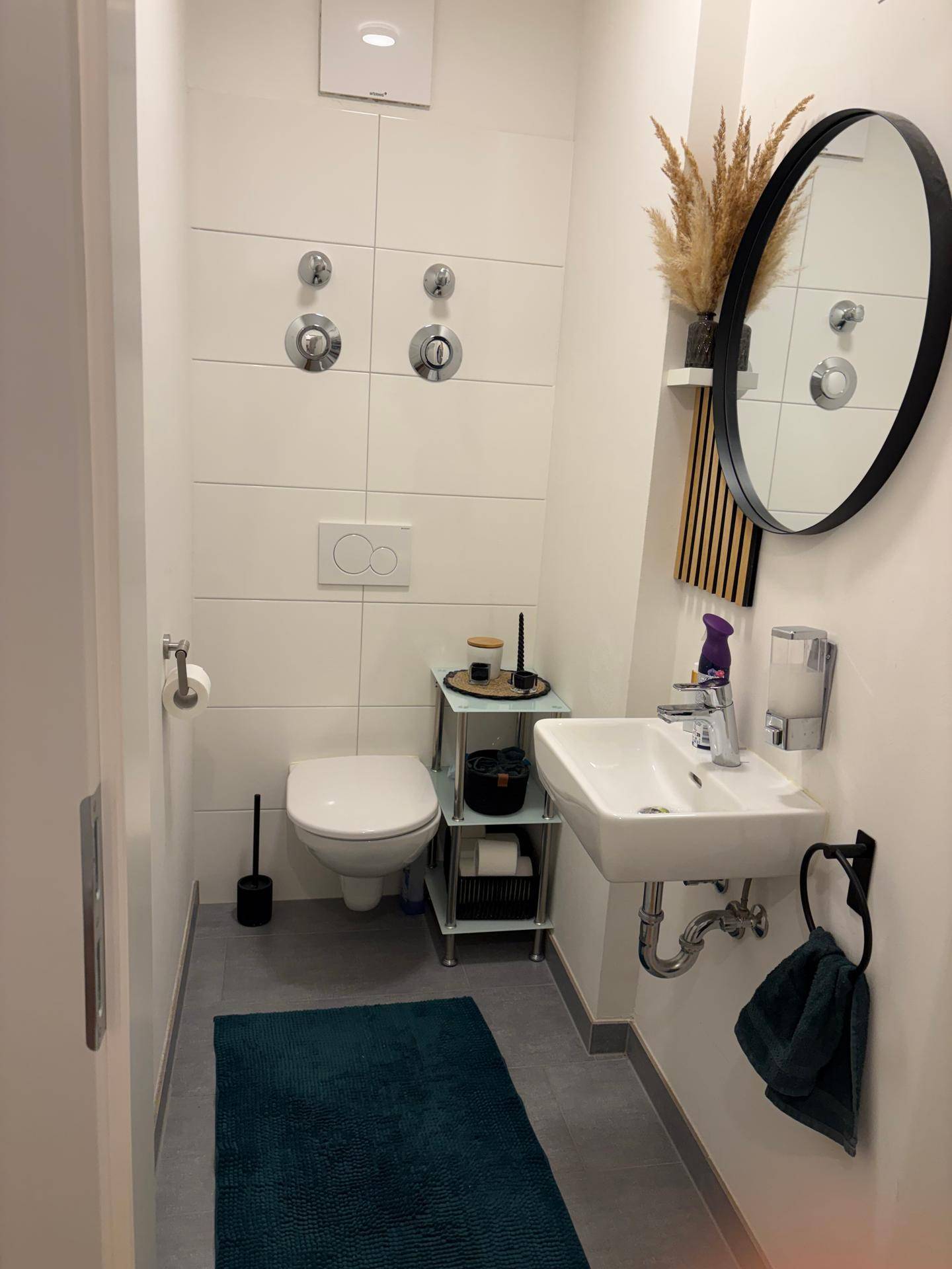 Modernes Gäste-WC mit Wand-WC, kleinem Waschbecken und stilvollem runden Spiegel.