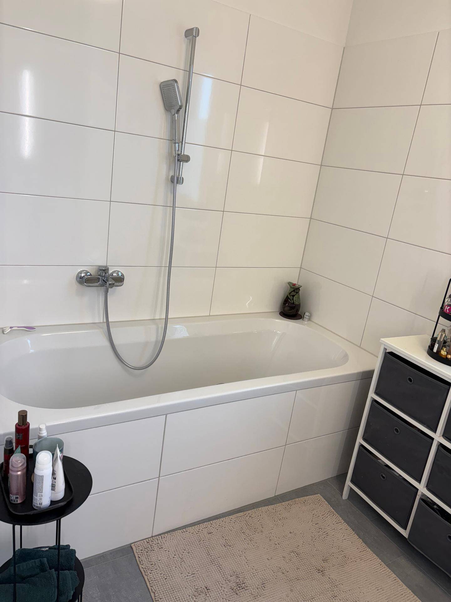 Badezimmer mit integrierter Badewanne, Duschfunktion und weißen Fliesen an Wänden und Boden.