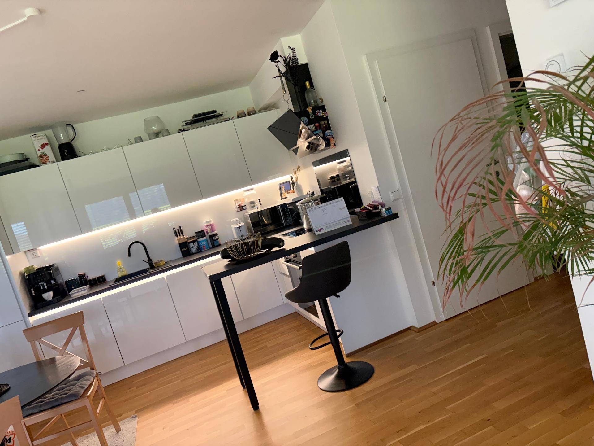 Moderne Küche mit weißen Hochglanzfronten, integrierter Beleuchtung und Frühstücksbar.