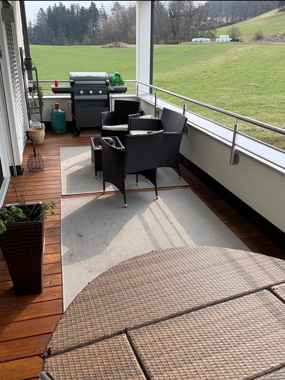 Geräumiger Balkon mit Sitzgelegenheiten, Grill und weitem Blick über grüne Wiesen.