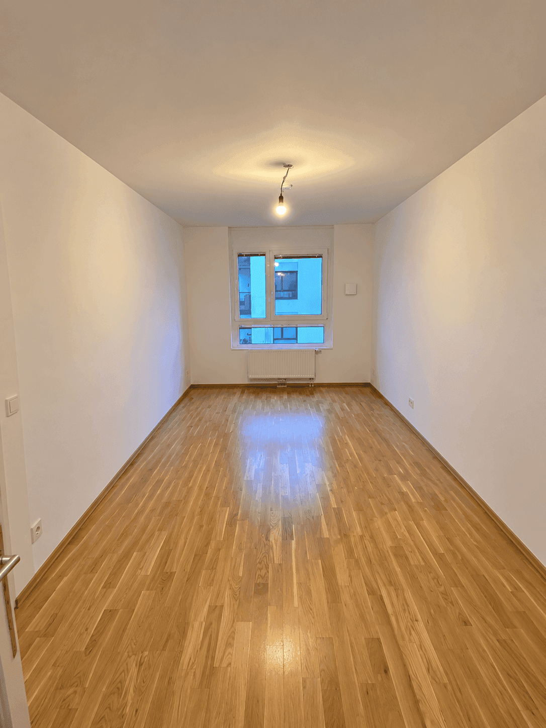 Leeres Zimmer mit Holzboden und Fenster, ideal als Schlaf- oder Arbeitszimmer.