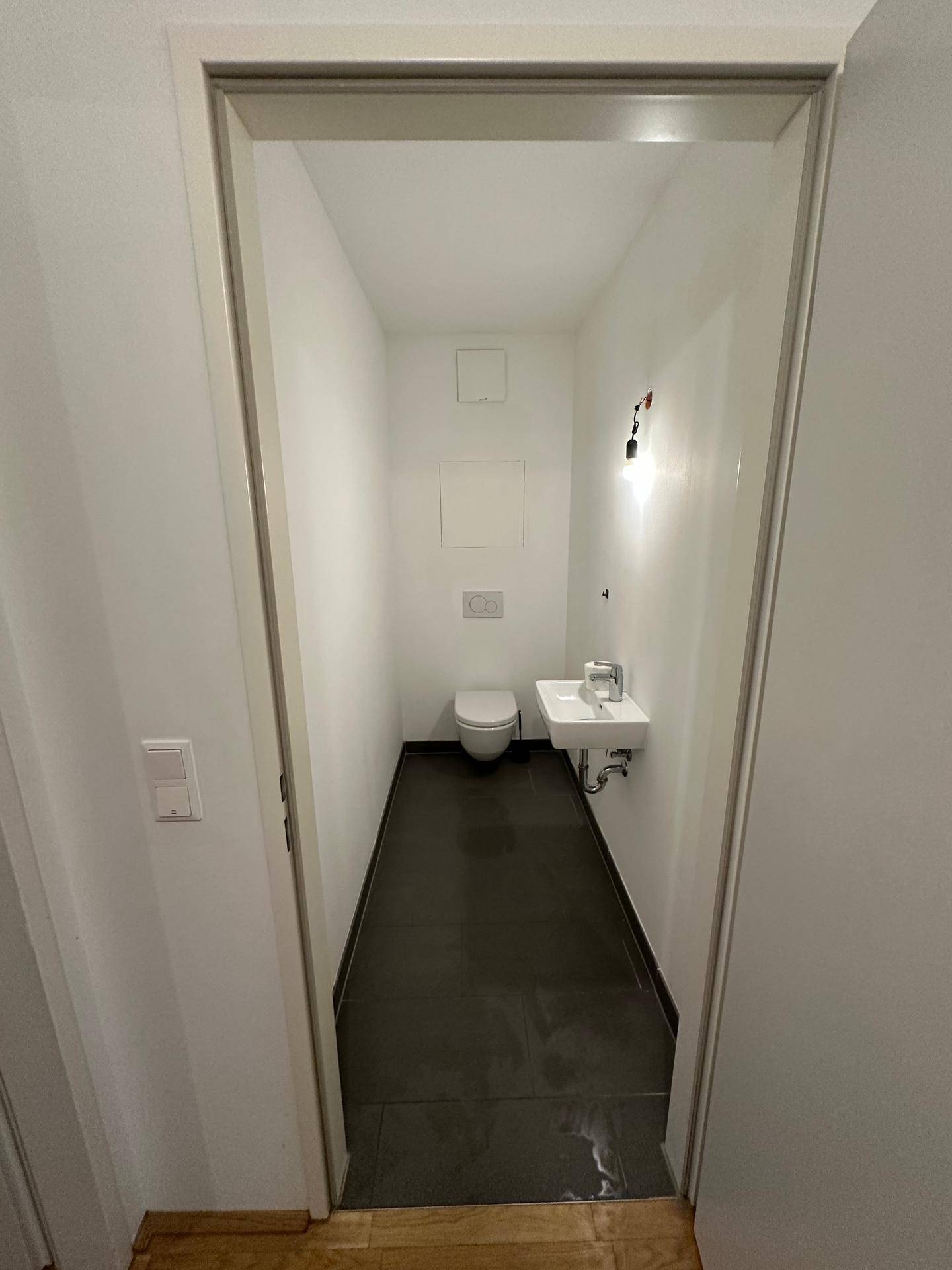 Separates Gäste-WC mit wandhängender Toilette und kleinem Waschbecken.