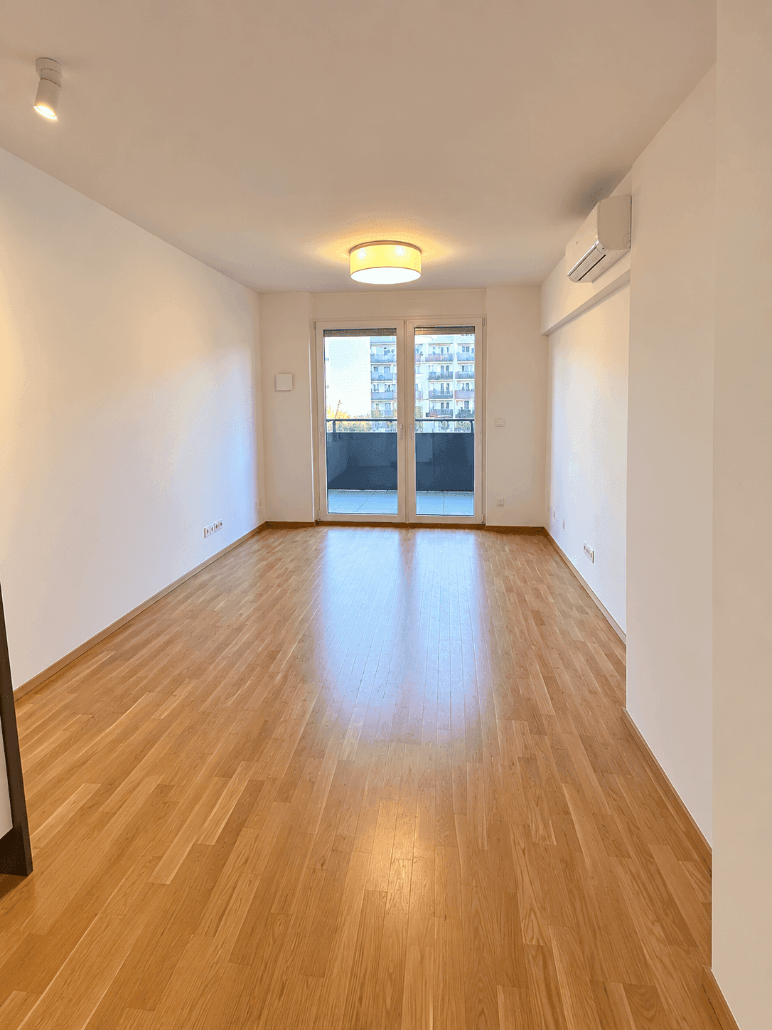 Helles Zimmer mit Holzboden, Zugang zum Balkon und Klimaanlage.