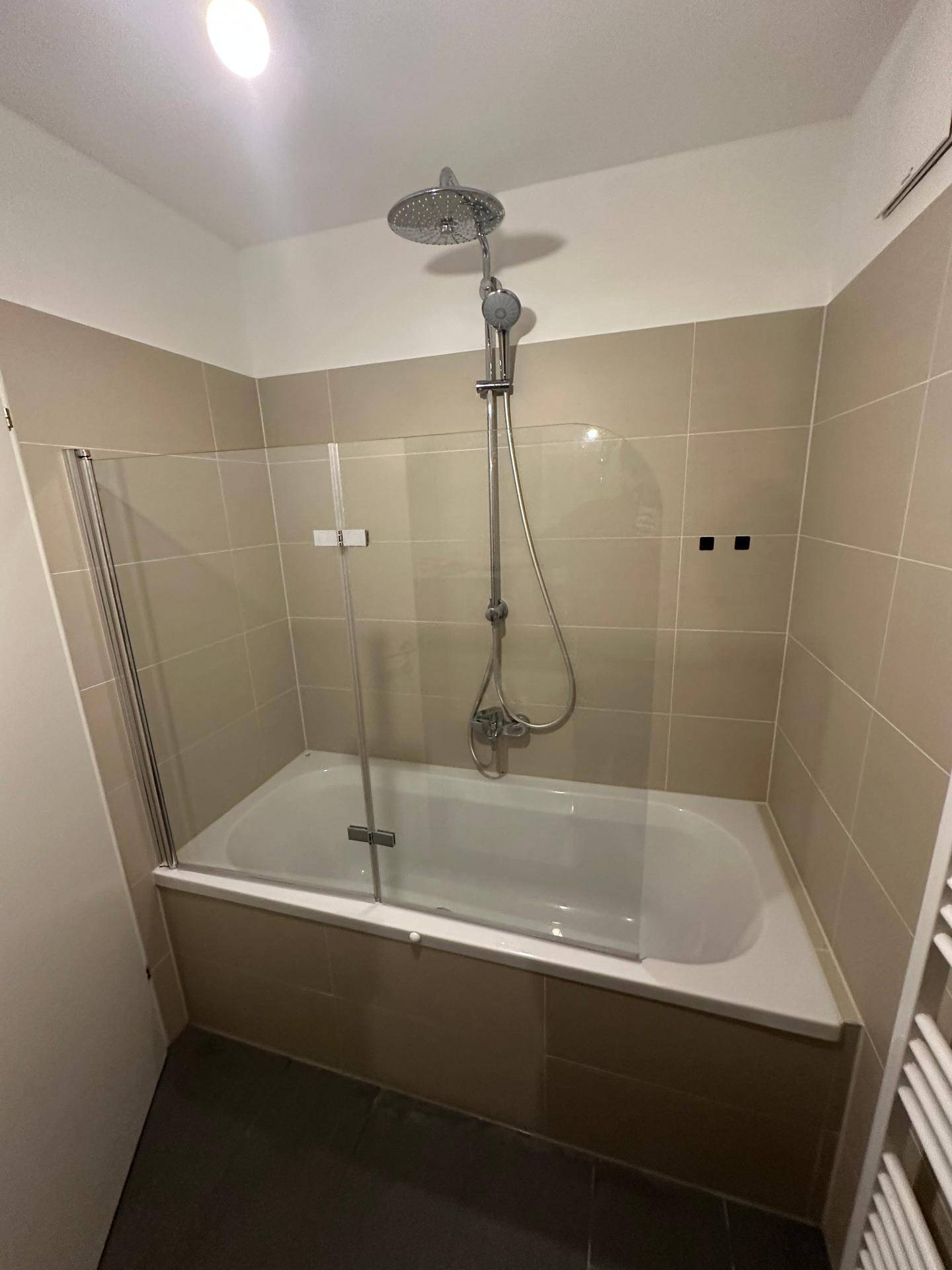 Badezimmer mit Badewanne, integrierter Dusche und modernen Fliesen.