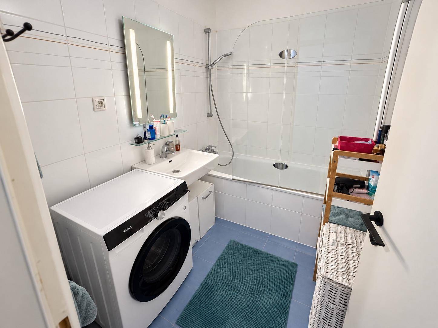 Helles Badezimmer mit Badewanne, Duschabtrennung, Waschbecken und Waschmaschine.