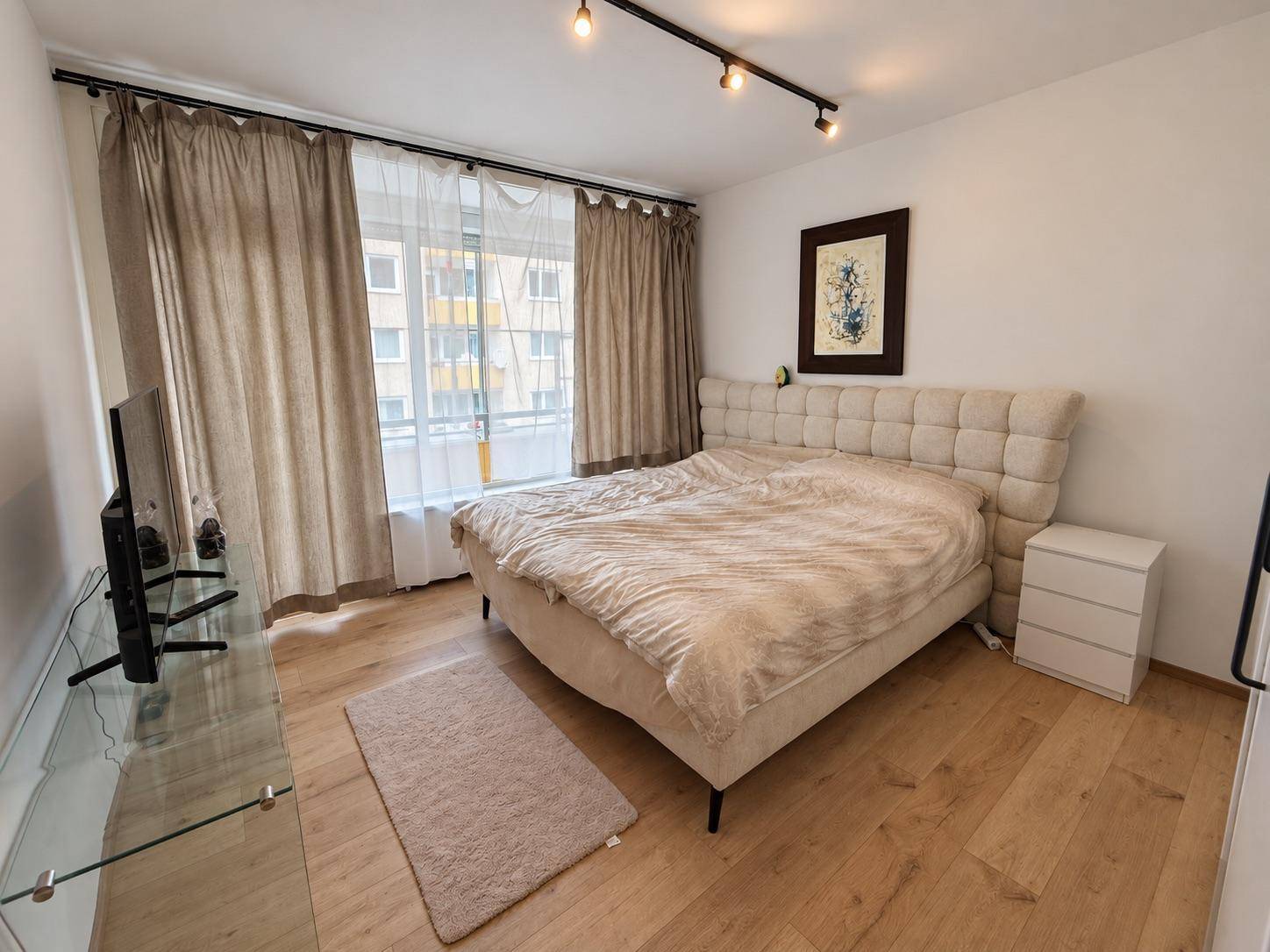 Gemütliches Schlafzimmer mit großem Doppelbett, Holzboden und Vorhängen am Fenster.