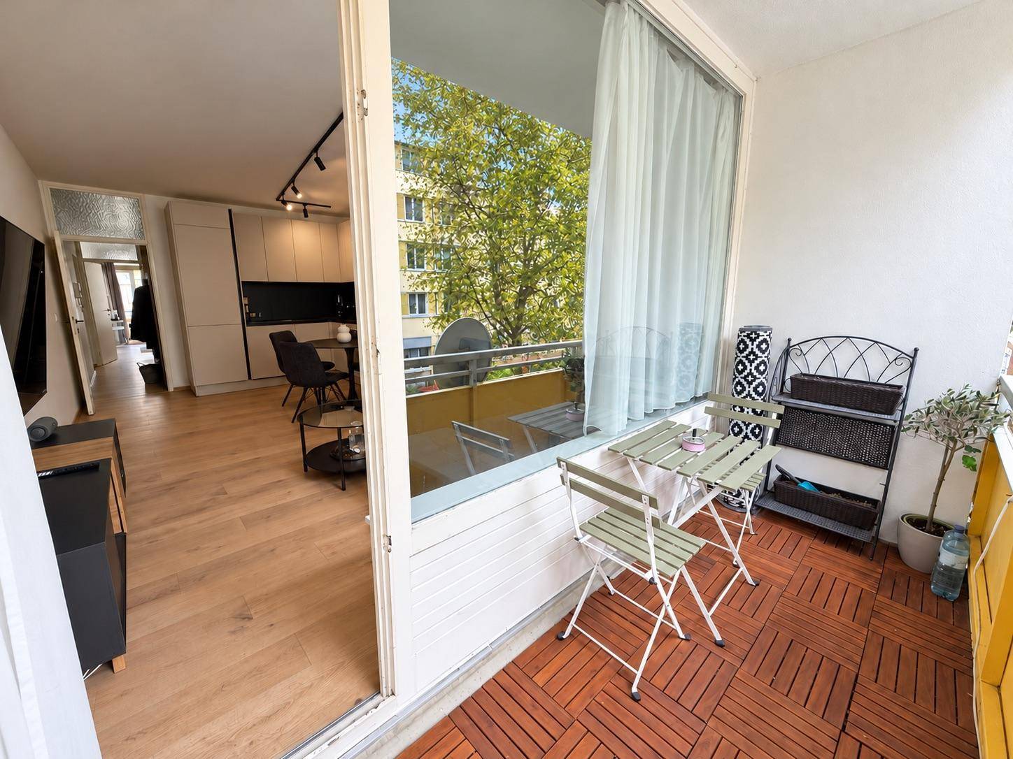 Sonniger Balkon mit Holzboden und Blick auf die grüne Umgebung sowie den Wohnbereich.