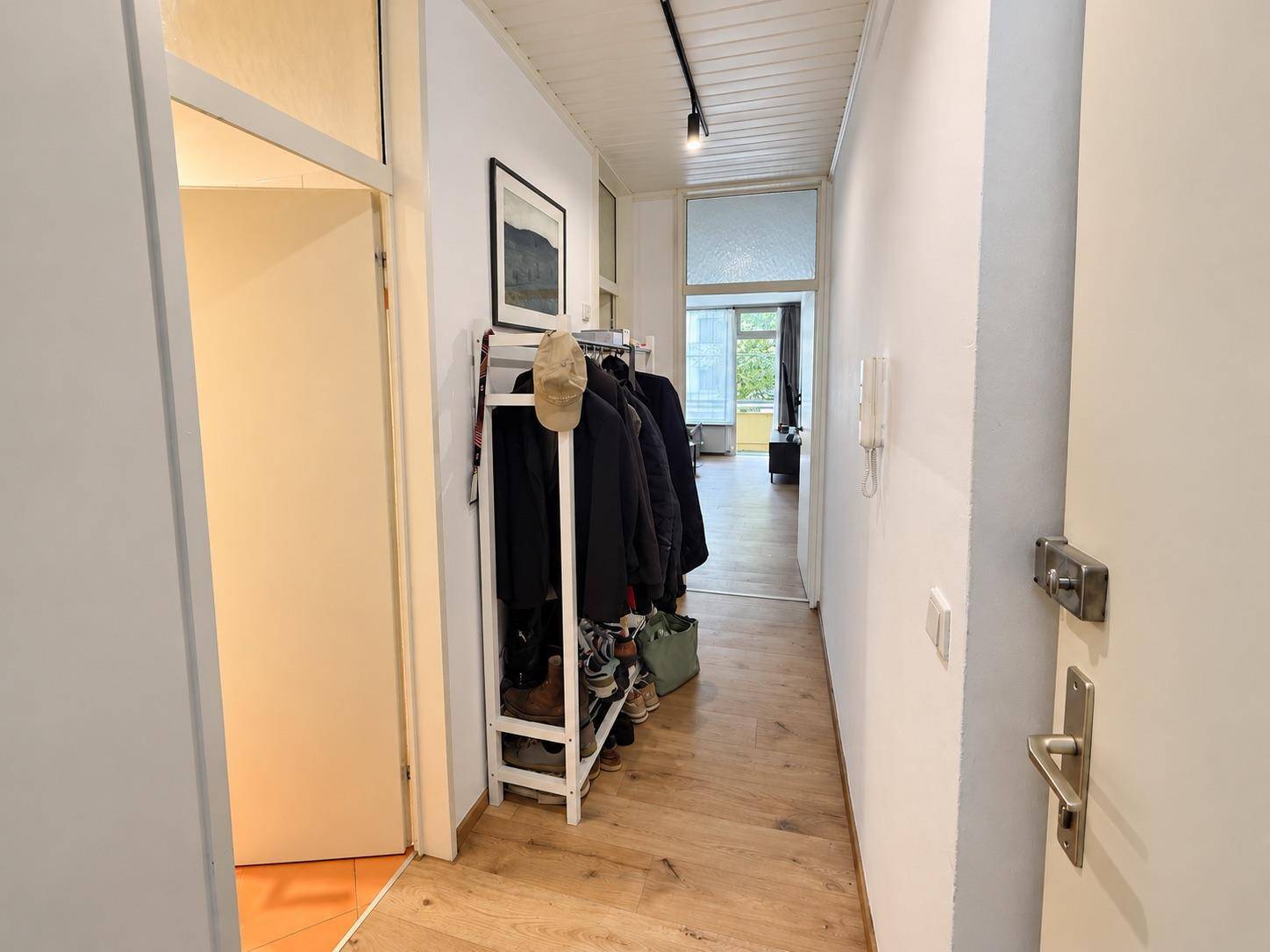 Schmaler Flur mit Holzboden, Garderobe und heller Beleuchtung, führt zu weiteren Räumen.
