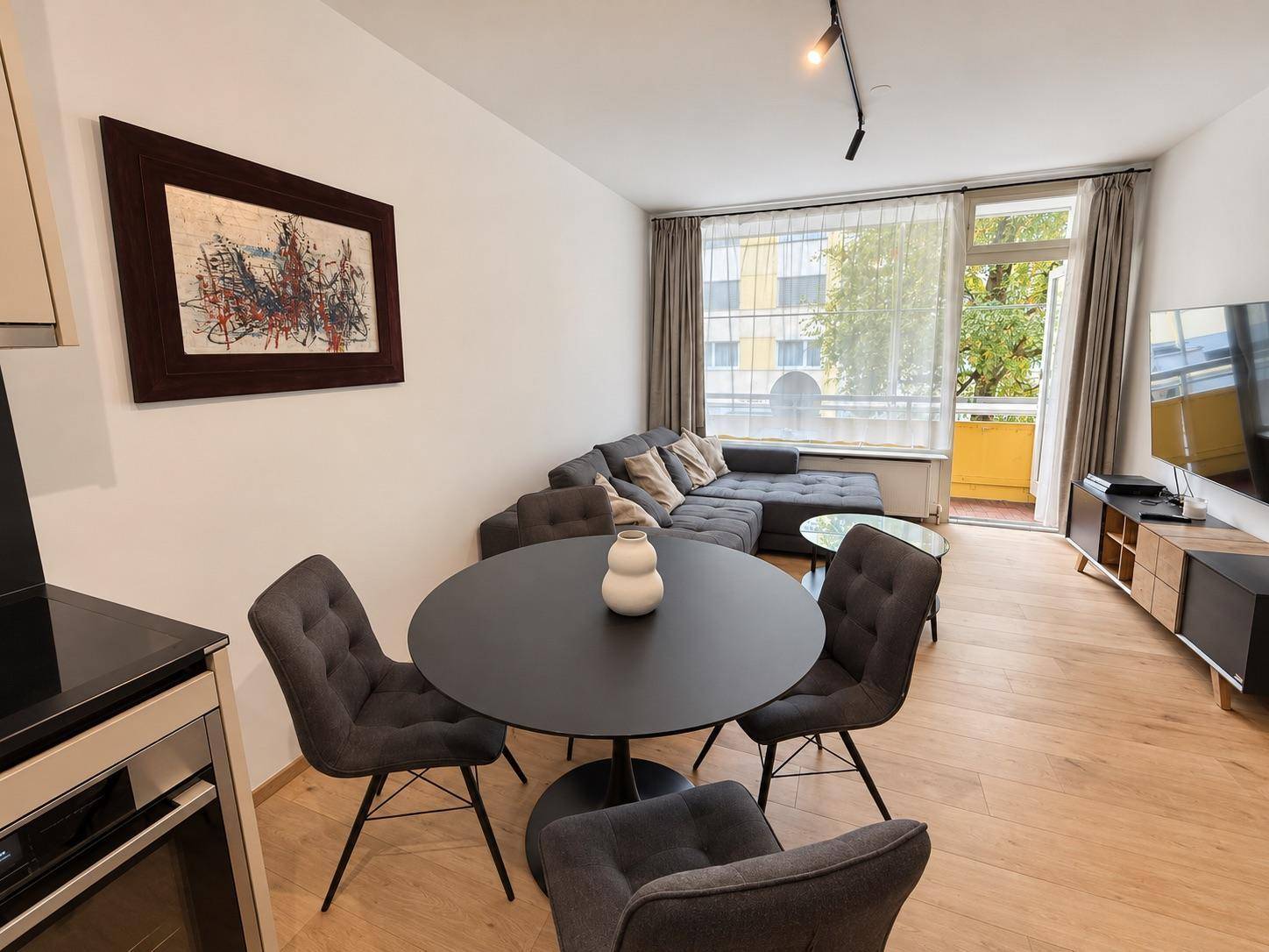 Gemütlicher Wohnbereich mit Esstisch, Sofa und Zugang zum Balkon, hell durch große Fenster.