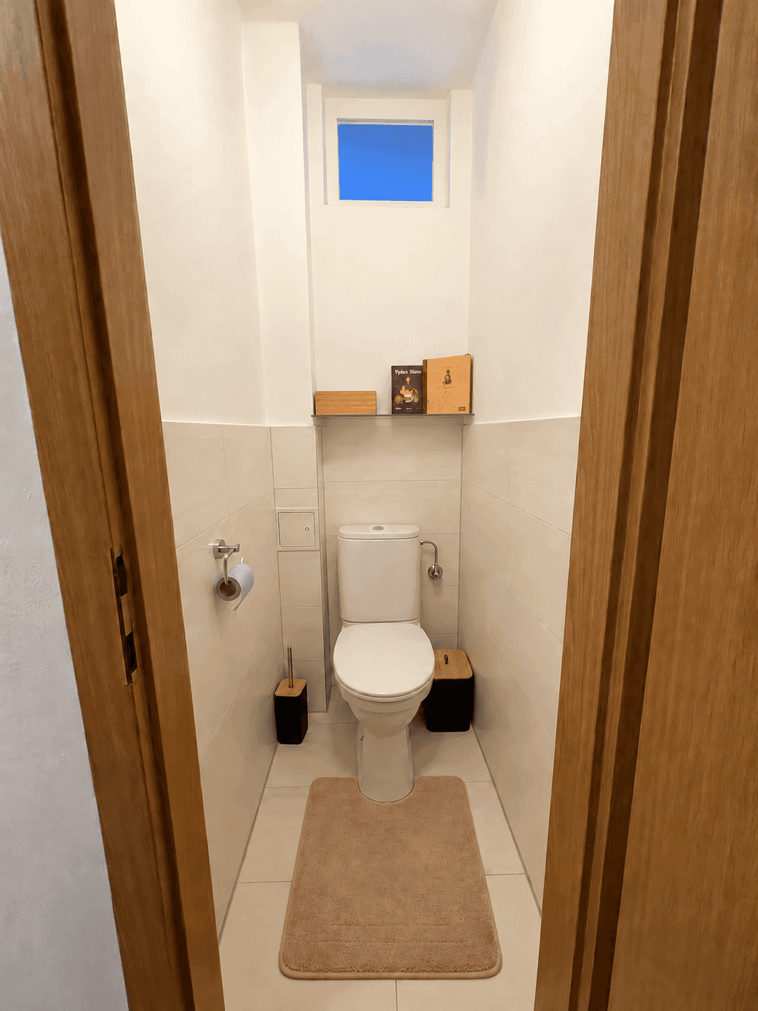 Separates WC mit Toilette, kleinem Fenster und Fliesenboden.