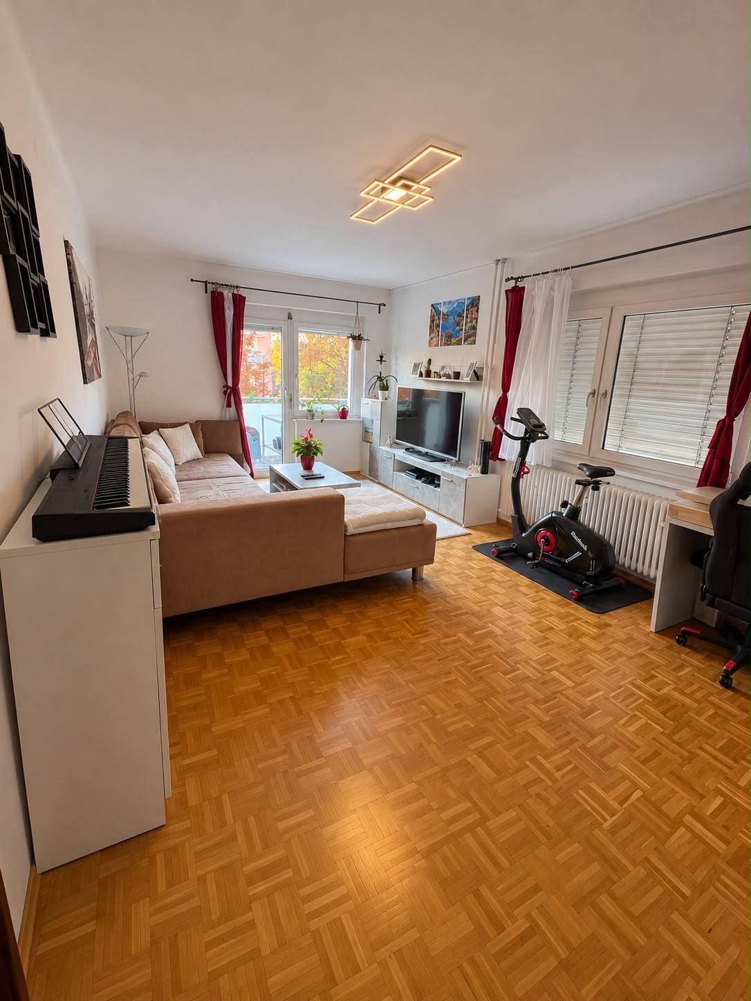 Helles Wohnzimmer mit bequemer Sitzecke, Fernseher und Parkettboden.