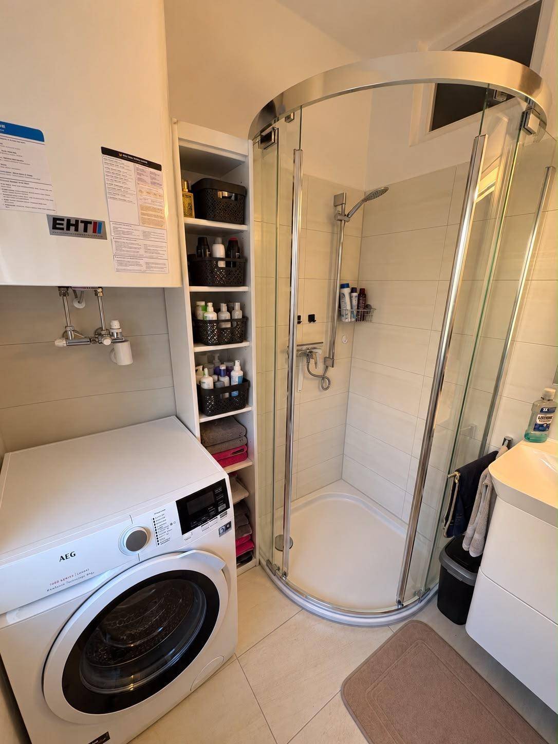 Funktionales Badezimmer mit Duschkabine, Waschmaschine und praktischen Regalen.