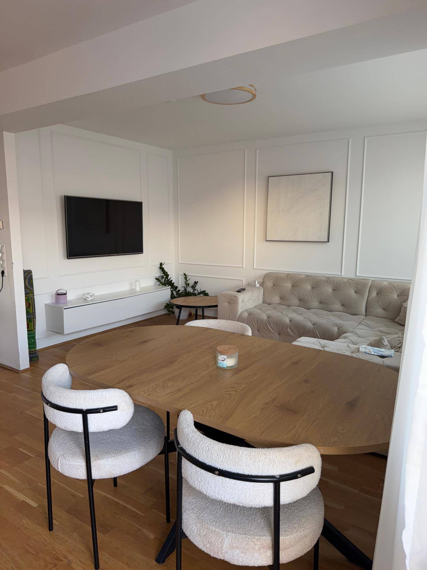 Offener Wohn- und Essbereich mit Holzboden, modernem Sofa und dekorativer Wandgestaltung.