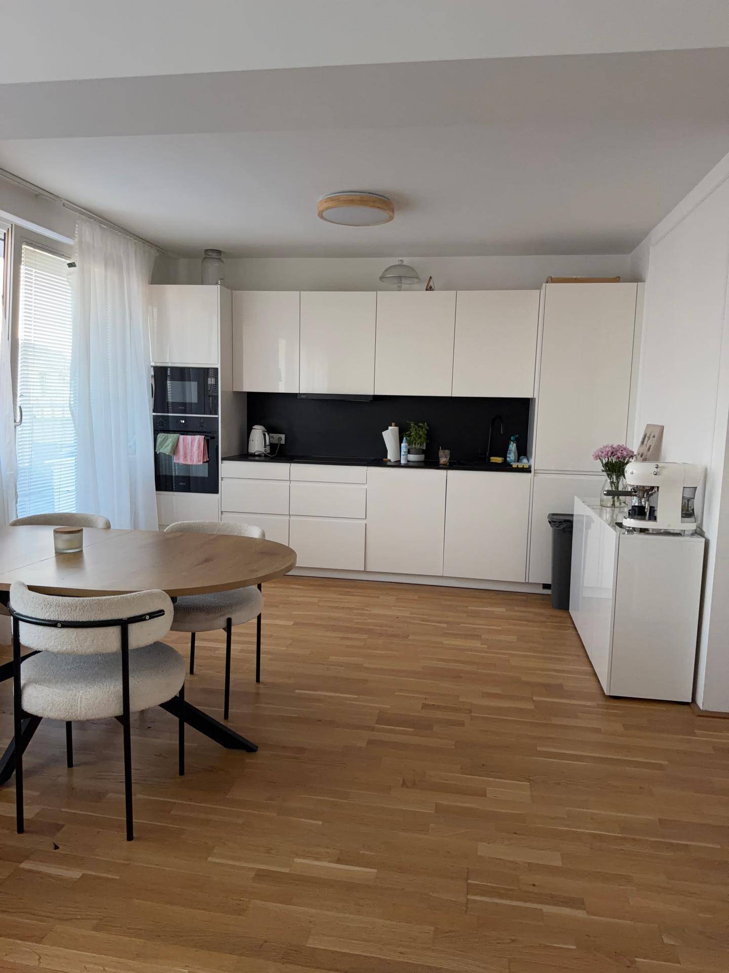 Helle, moderne Küche mit weißen Schränken, Holzboden und einem runden Esstisch.