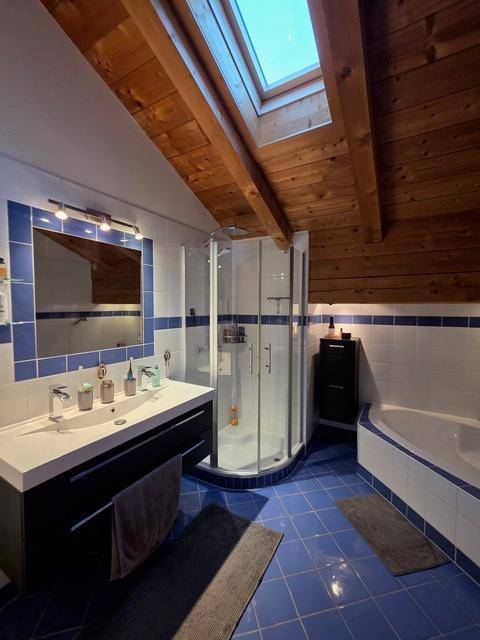 Geräumiges Badezimmer mit blauen Fliesen, Doppelwaschbecken, Dusche, Badewanne und Dachfenster.