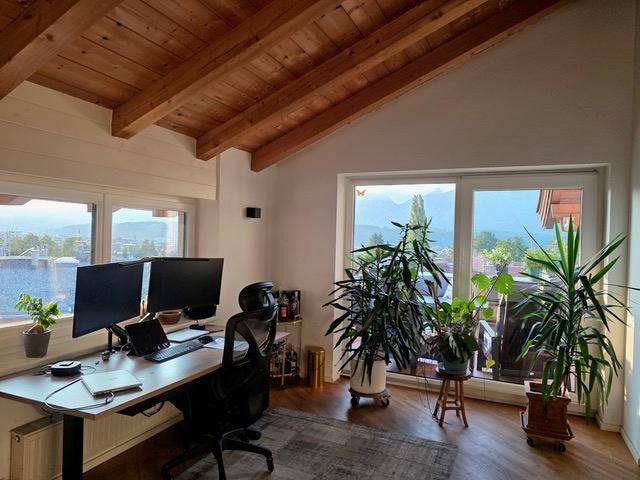 Helles Heimbüro mit Holzbalkendecke, großem Fenster und inspirierendem Bergblick.
