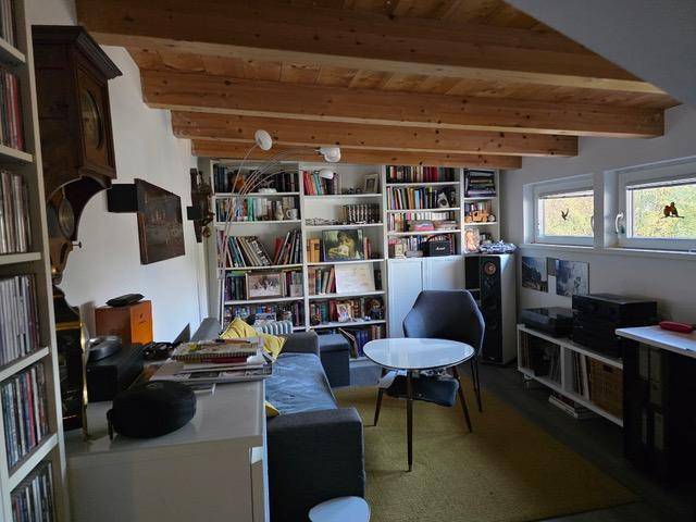 Gemütlicher Wohnbereich mit Bücherregalen, Sofa und rustikaler Holzbalkendecke.