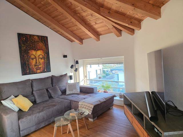 Gemütliches Wohnzimmer mit großem Sofa, Holzbalkendecke und viel Tageslicht.