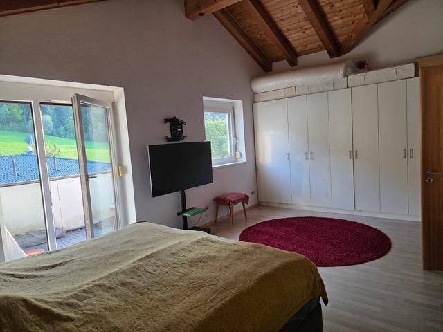 Helles Schlafzimmer mit Einbauschränken, Fernseher und direktem Zugang zum Balkon.