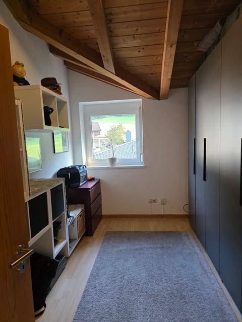 Kleines Zimmer mit Fenster, Einbauschränken und sichtbaren Holzbalken an der Decke.