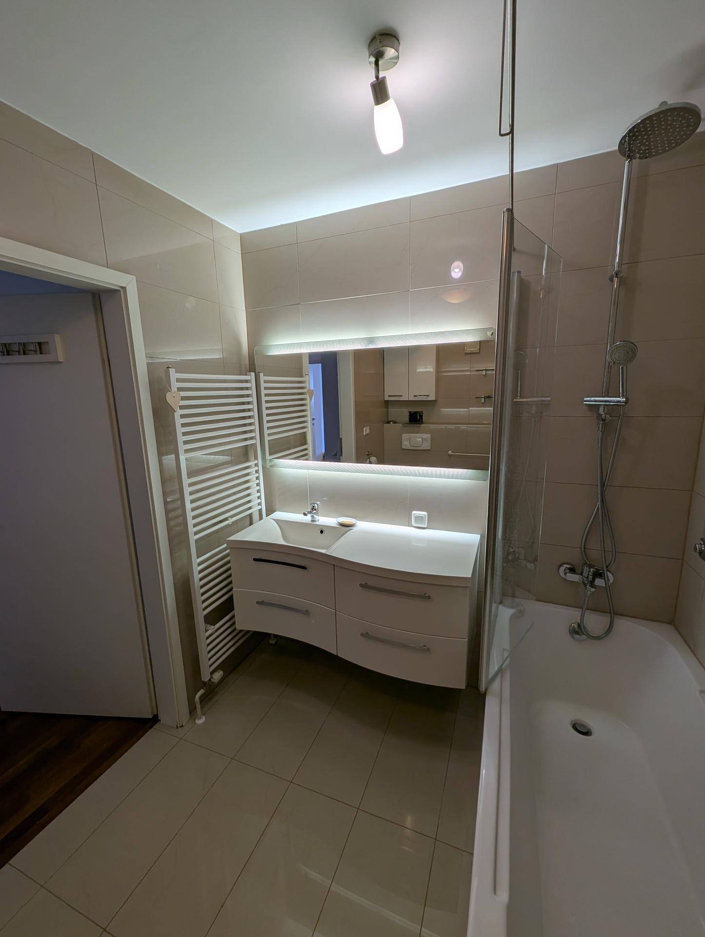 Modernes Badezimmer mit beigen Fliesen, Badewanne, Dusche und einem beheizten Handtuchhalter an der Wand.