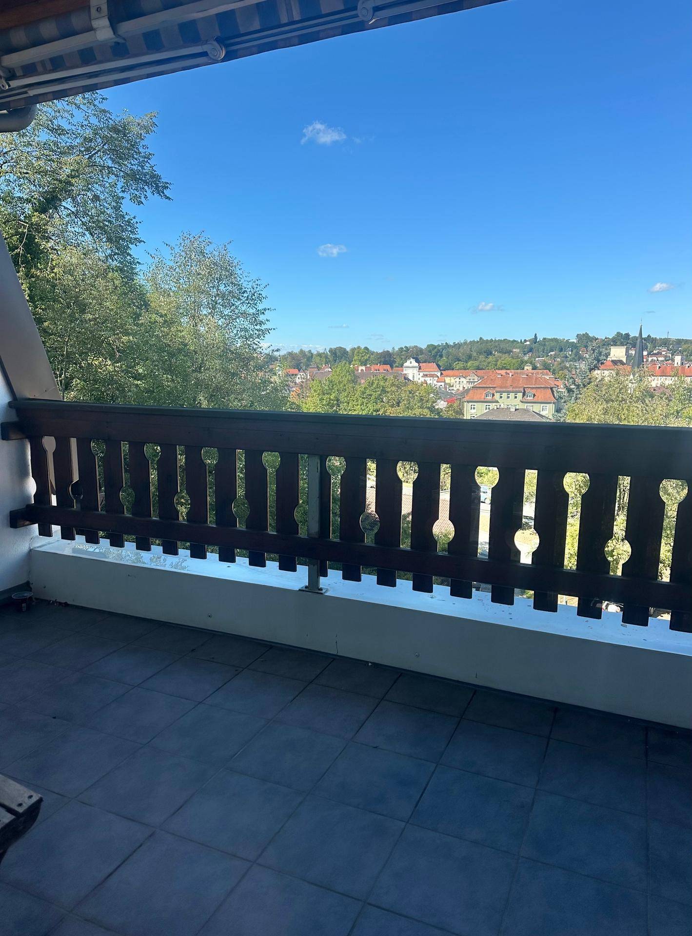 Geräumiger Balkon mit Holzbalkongeländer und Fliesenboden, bietet einen weiten Blick über die Stadt.