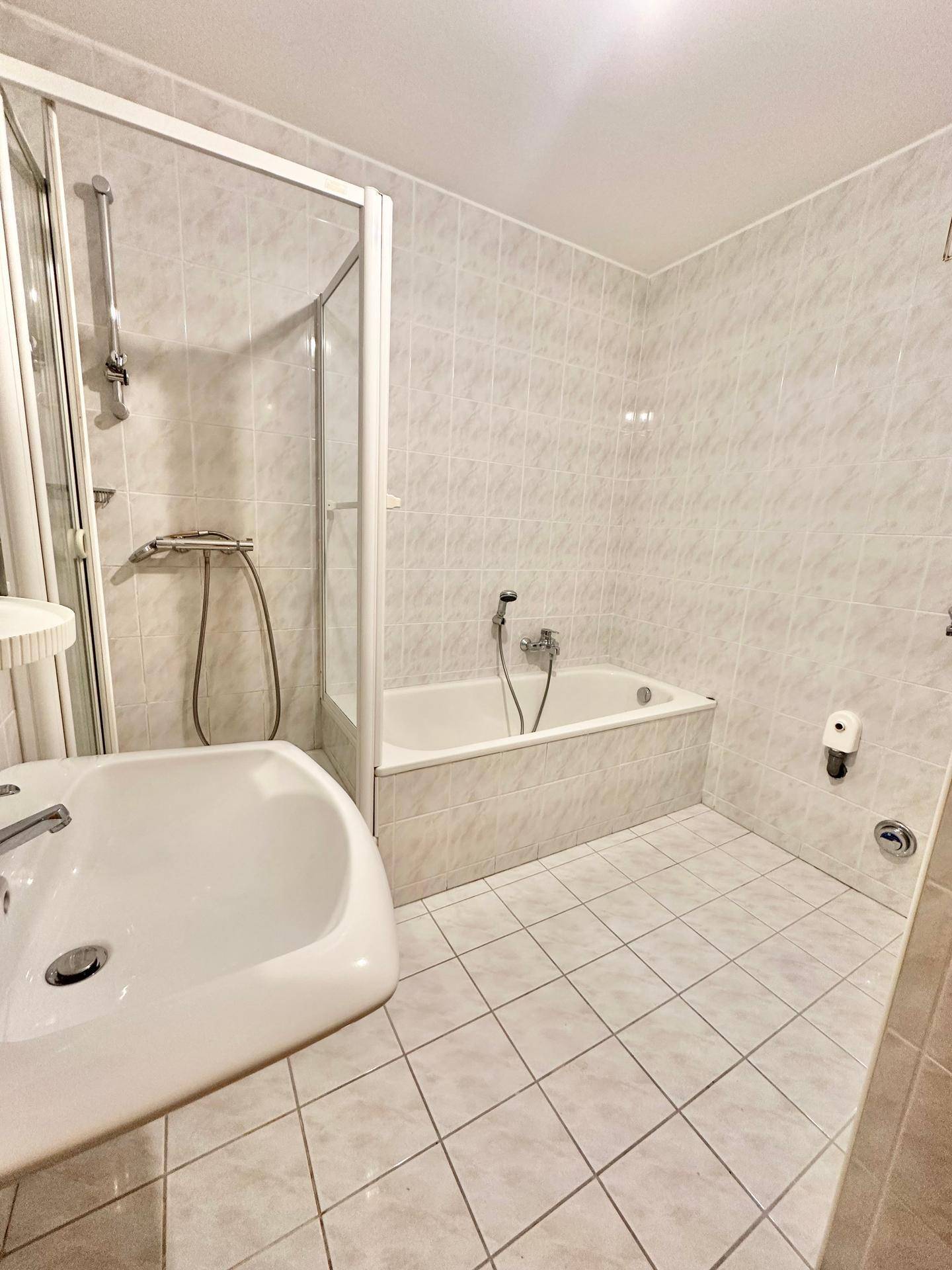 Gefliestes Badezimmer mit Badewanne und Duschkabine, ausgestattet mit einem einzelnen Waschbecken.