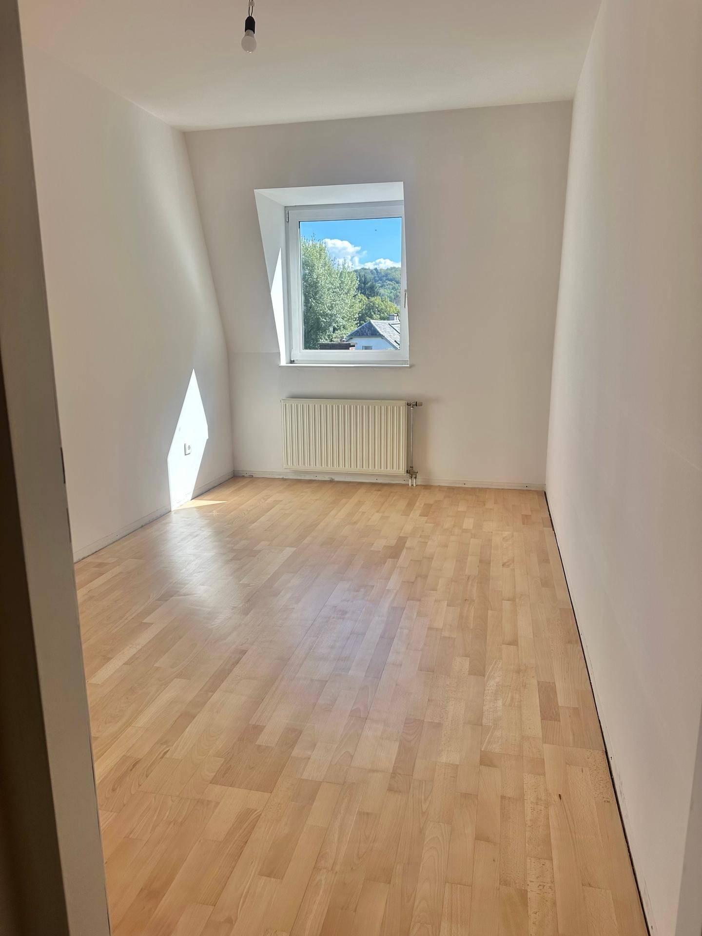 Freundliches Schlafzimmer mit hellem Holzfußboden und Dachschrägenfenster, das viel Sonnenlicht einfängt.