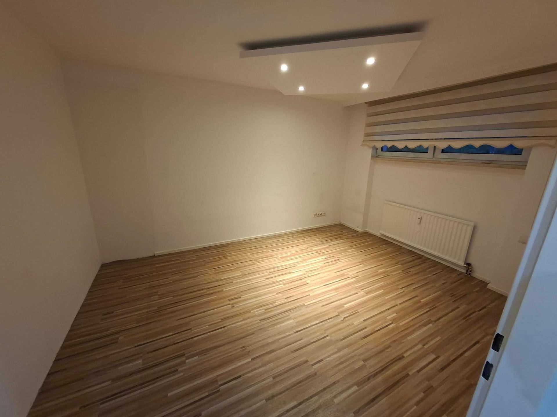 Leeres Zimmer mit Laminatboden und Fenster, bereit für neue Einrichtungsideen.