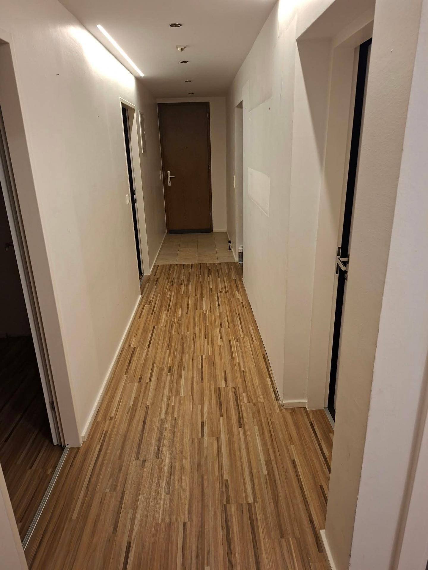 Heller Flur mit Laminatboden und integrierter Deckenbeleuchtung, der zu weiteren Räumen führt.