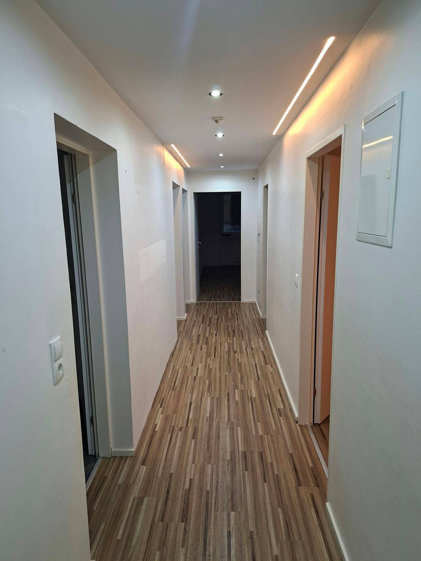 Langer, heller Flur mit Laminatboden und moderner LED-Beleuchtung.