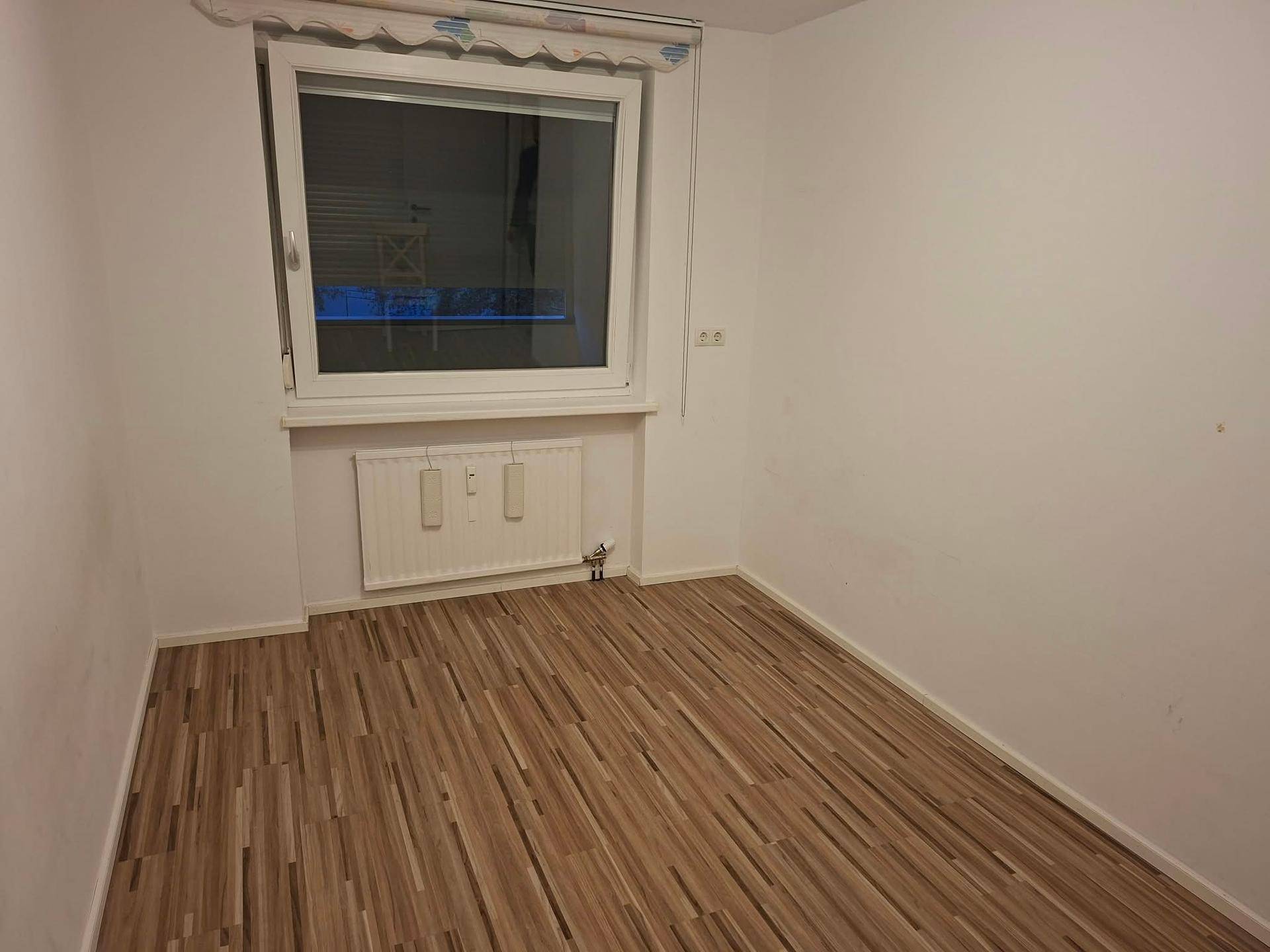 Leeres Zimmer mit Laminatboden und großem Fenster, bietet viel Tageslicht.