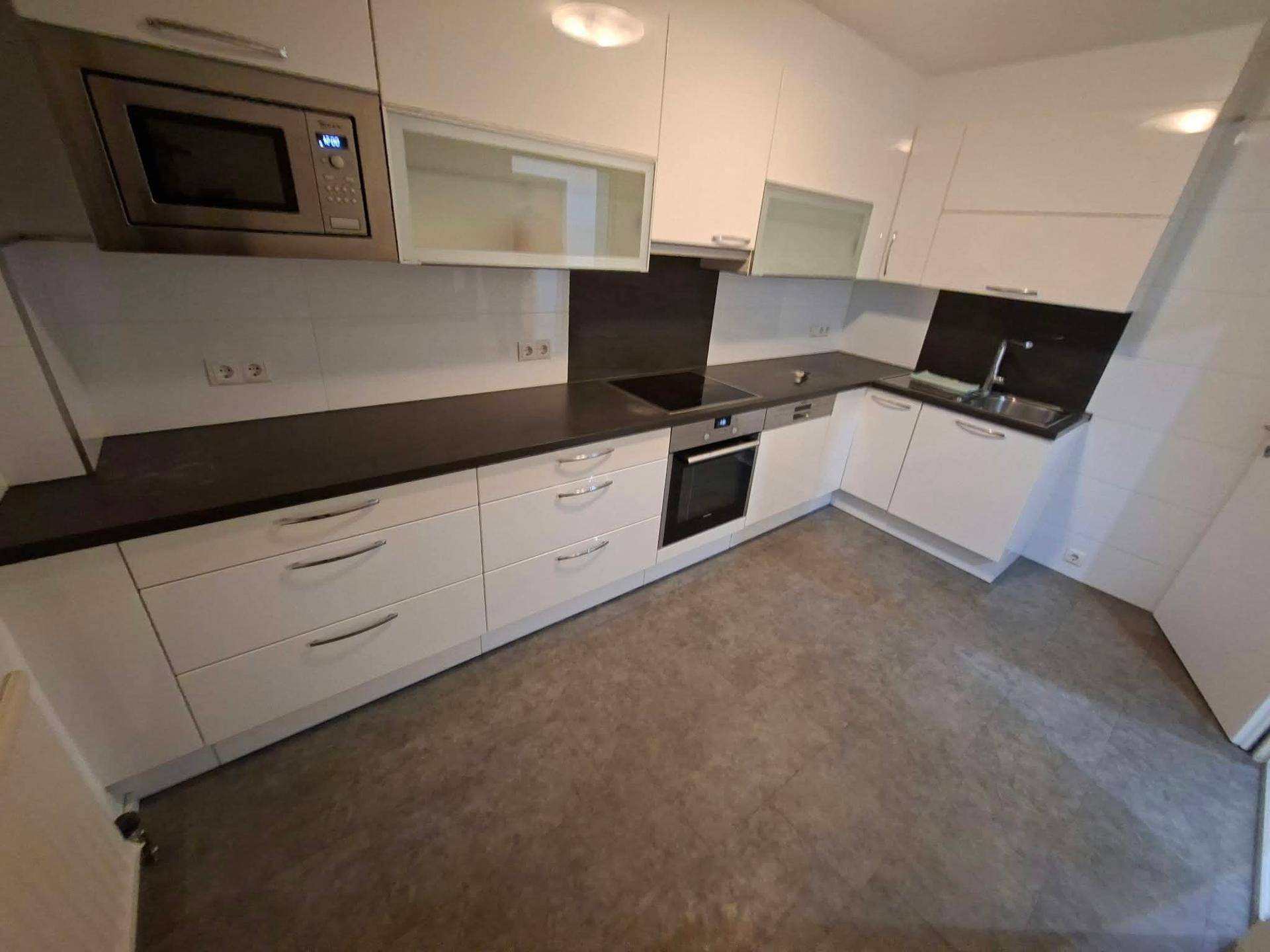 Moderne Einbauküche mit weißen Fronten, dunkler Arbeitsplatte und integrierten Geräten.