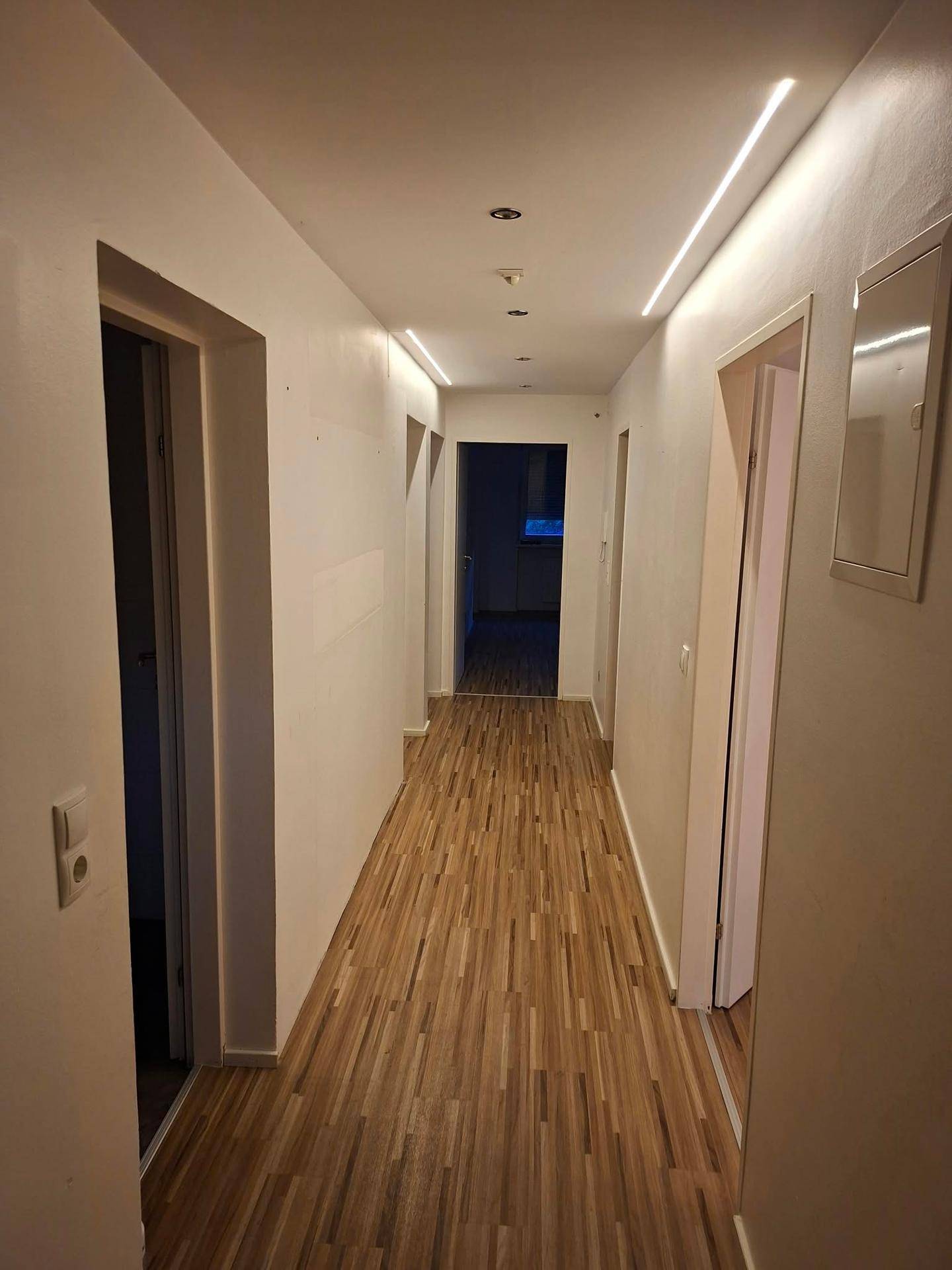 Heller Flur mit Laminatboden und integrierter Deckenbeleuchtung, der zu den Zimmern führt.