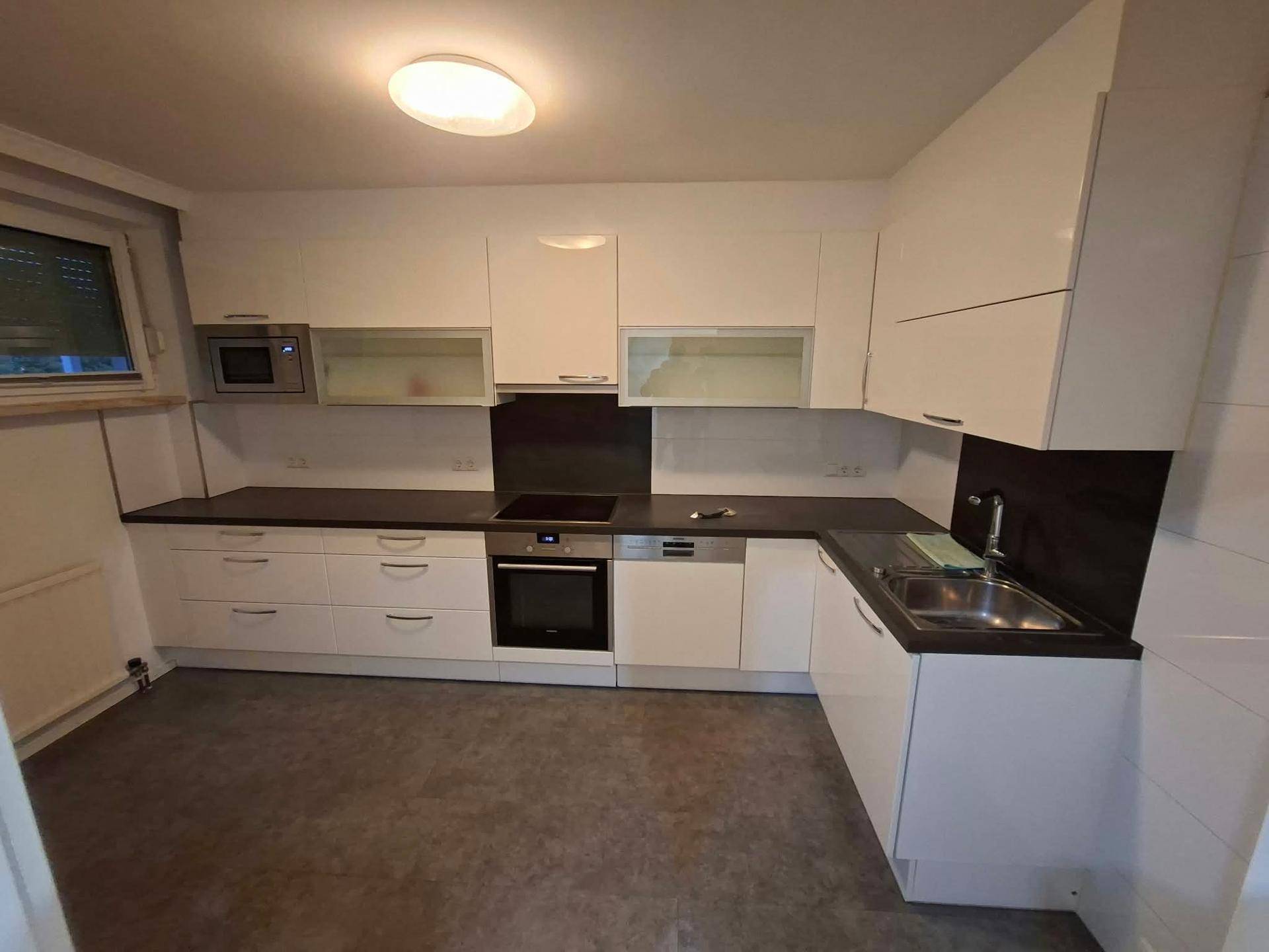Funktionale Einbauküche mit weißen Schränken, dunkler Arbeitsplatte und Fenster.